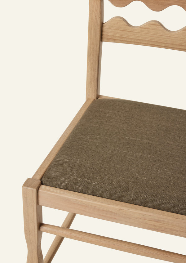 Detailed view of the Freda Razor Dining Chair in natural oak with an upholstered performance olive linen seat. The hand-carved scalloped backrest adds a playful yet timeless detail.