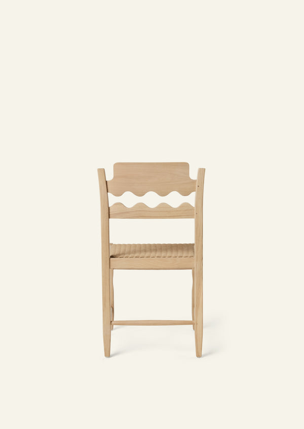 Back view of the Freda Razor Dining Chair in natural oak with a woven paper cord seat. The hand-carved scalloped backrest adds a playful yet timeless detail.