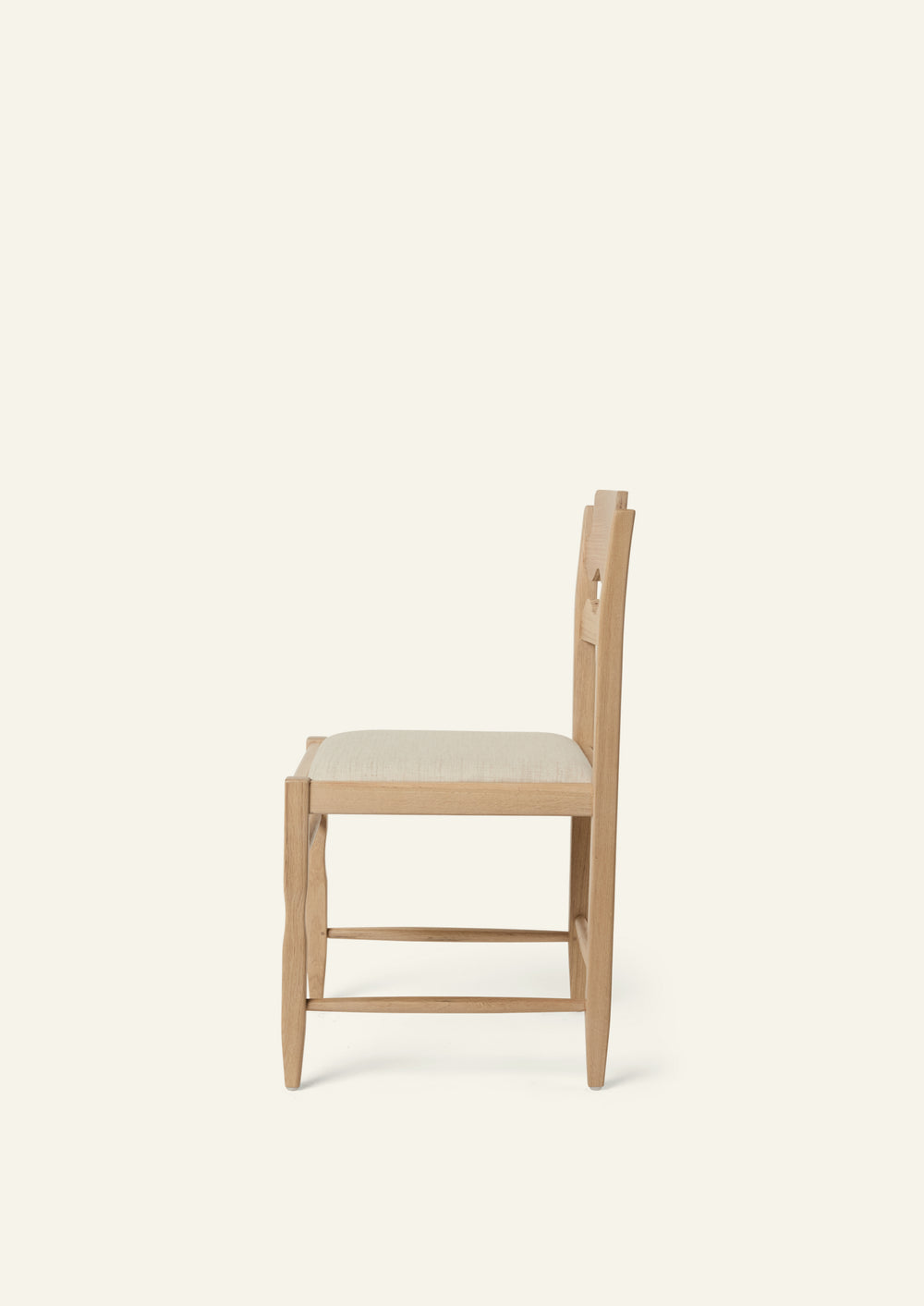 Side view of the Freda Razor Dining Chair in natural oak with an upholstered performance sand linen seat, shown from an angled front view on a neutral background. The hand-carved scalloped backrest adds a playful yet timeless detail.