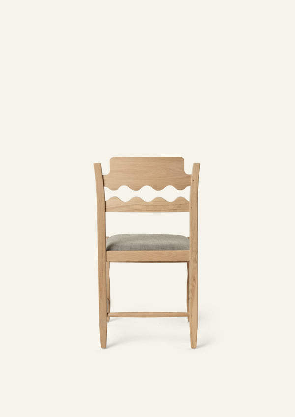 Back view of the Freda Razor Dining Chair in natural oak with an upholstered performance slate linen seat. The hand-carved scalloped backrest adds a playful yet timeless detail.
