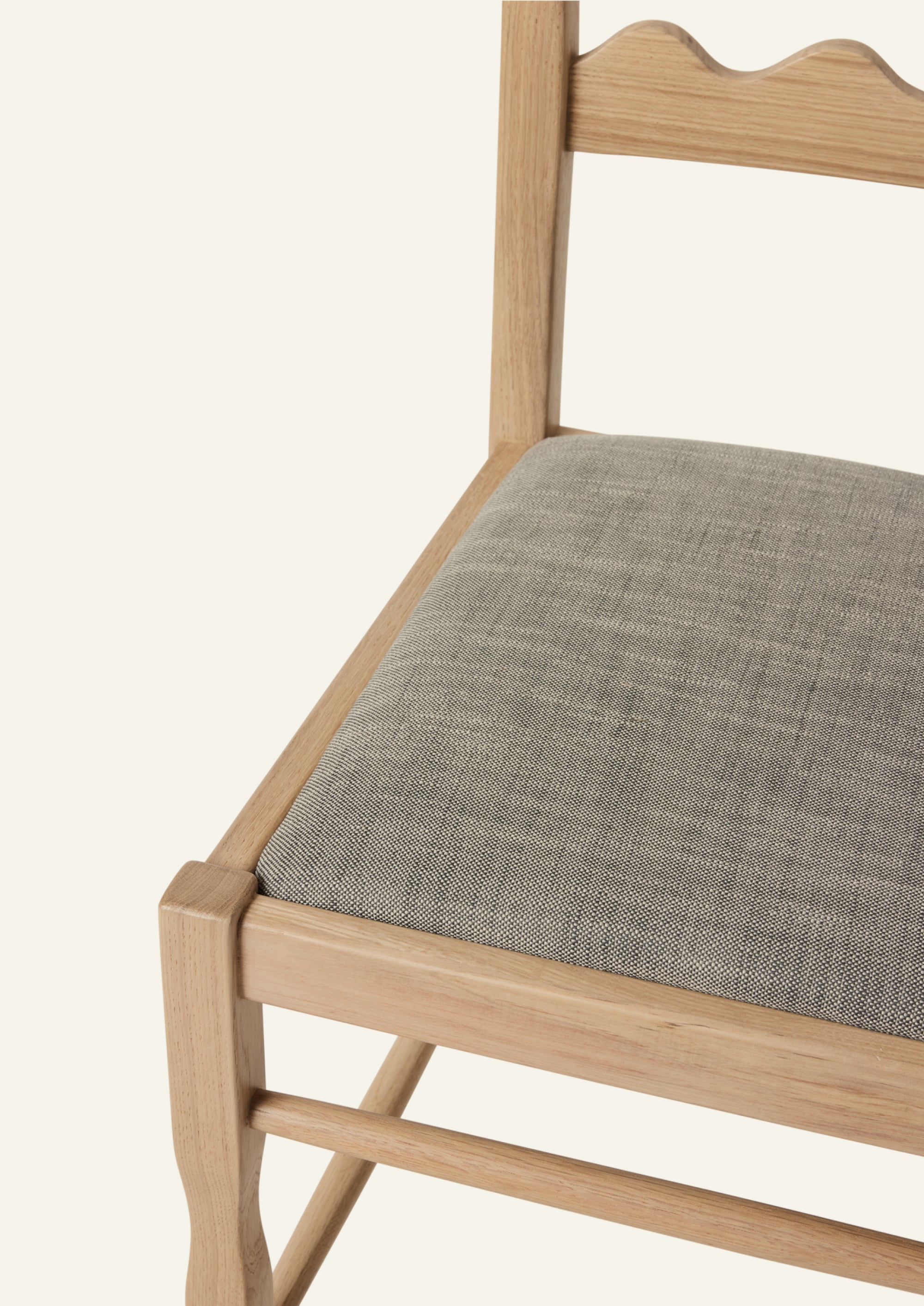 Detailed view of the Freda Razor Dining Chair in natural oak with an upholstered performance slate linen seat. The hand-carved scalloped backrest adds a playful yet timeless detail.