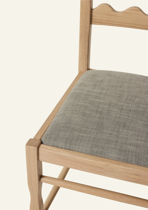 Detailed view of the Freda Razor Dining Chair in natural oak with an upholstered performance slate linen seat. The hand-carved scalloped backrest adds a playful yet timeless detail.