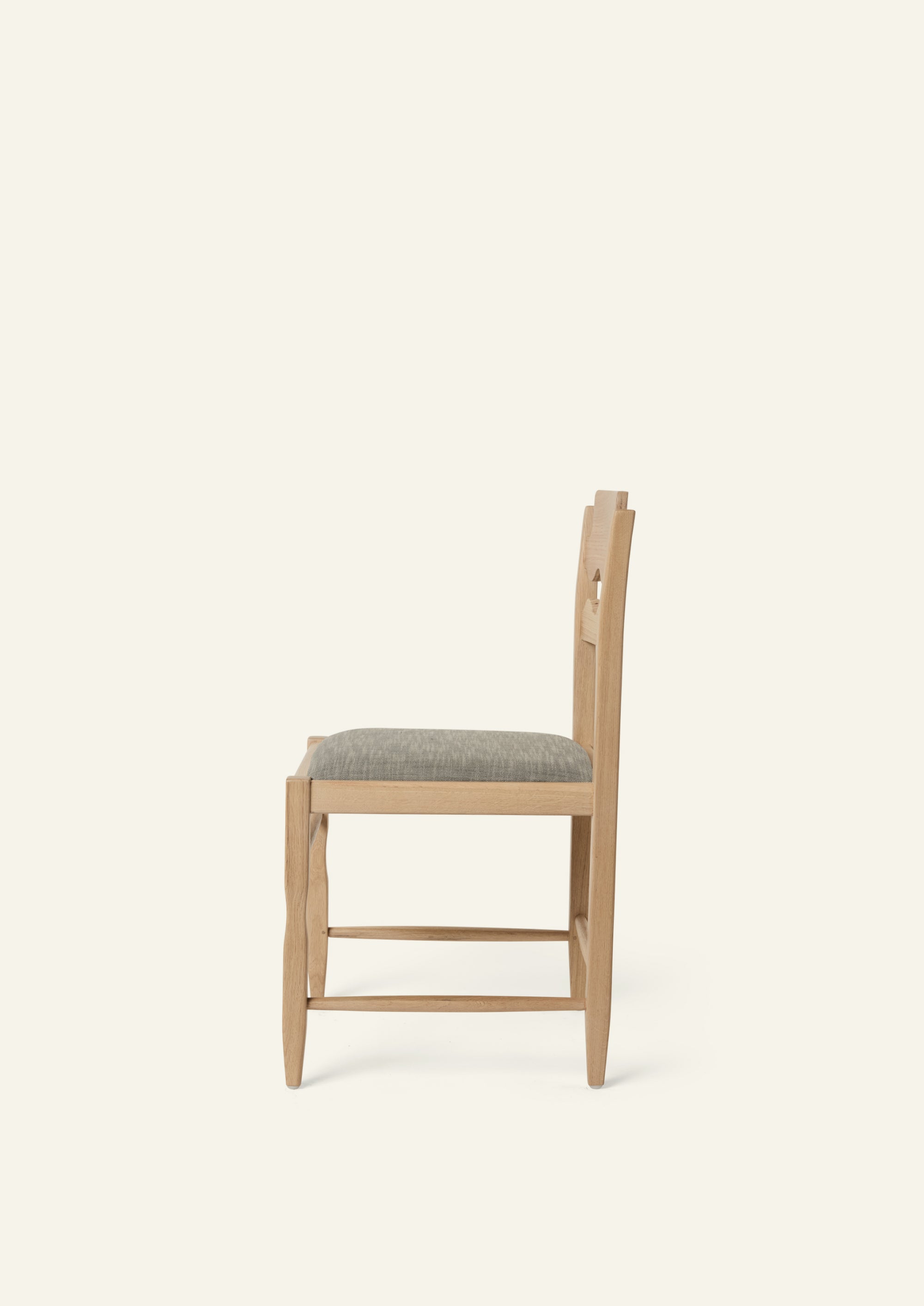 Side view of the Freda Razor Dining Chair in natural oak with an upholstered performance slate linen seat. The hand-carved scalloped backrest adds a playful yet timeless detail.