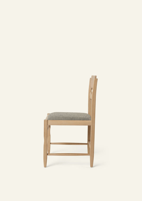 Side view of the Freda Razor Dining Chair in natural oak with an upholstered performance slate linen seat. The hand-carved scalloped backrest adds a playful yet timeless detail.