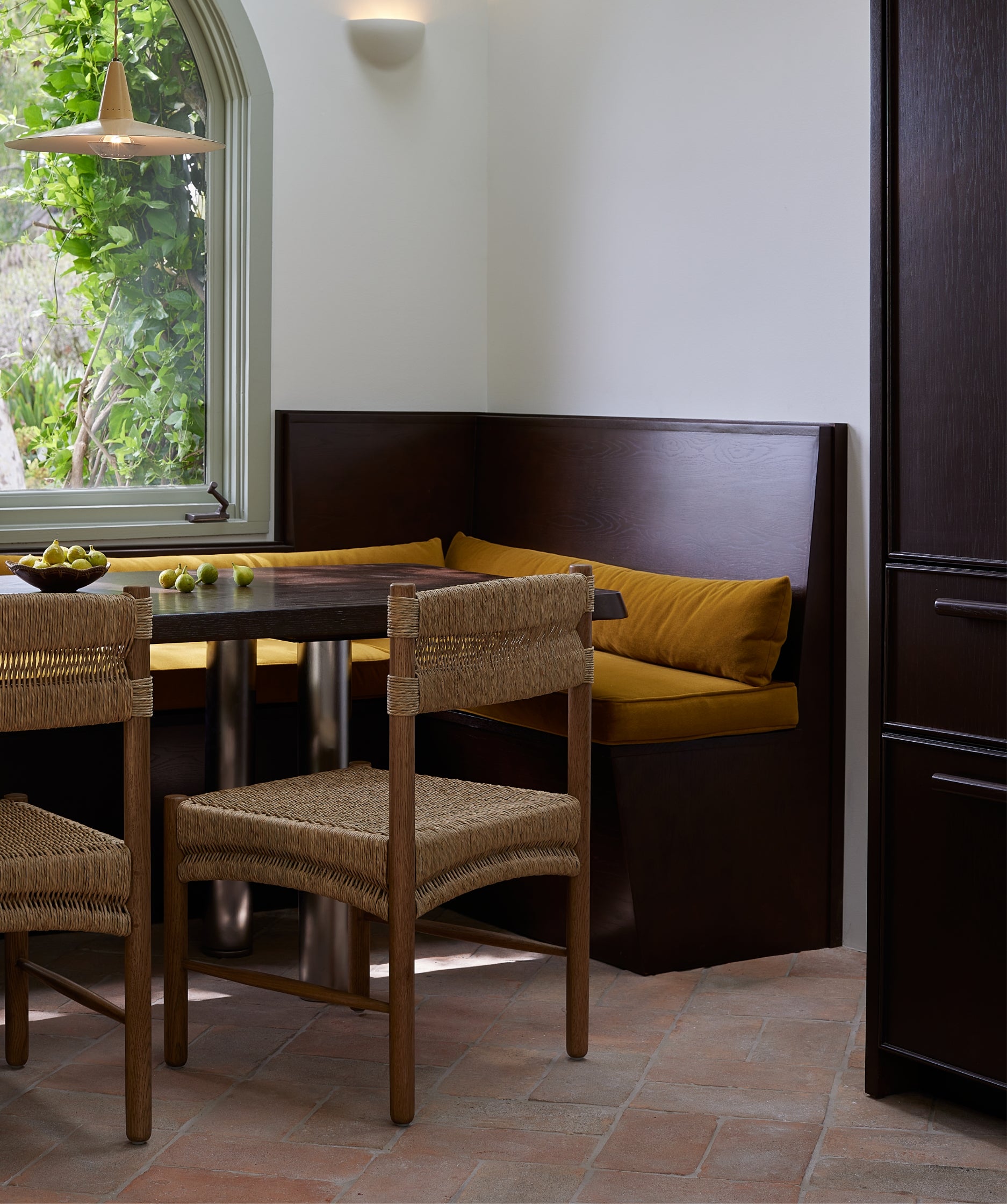 Dining area with Suma dining chairs, a table, and a bench with yellow cushions near a window.