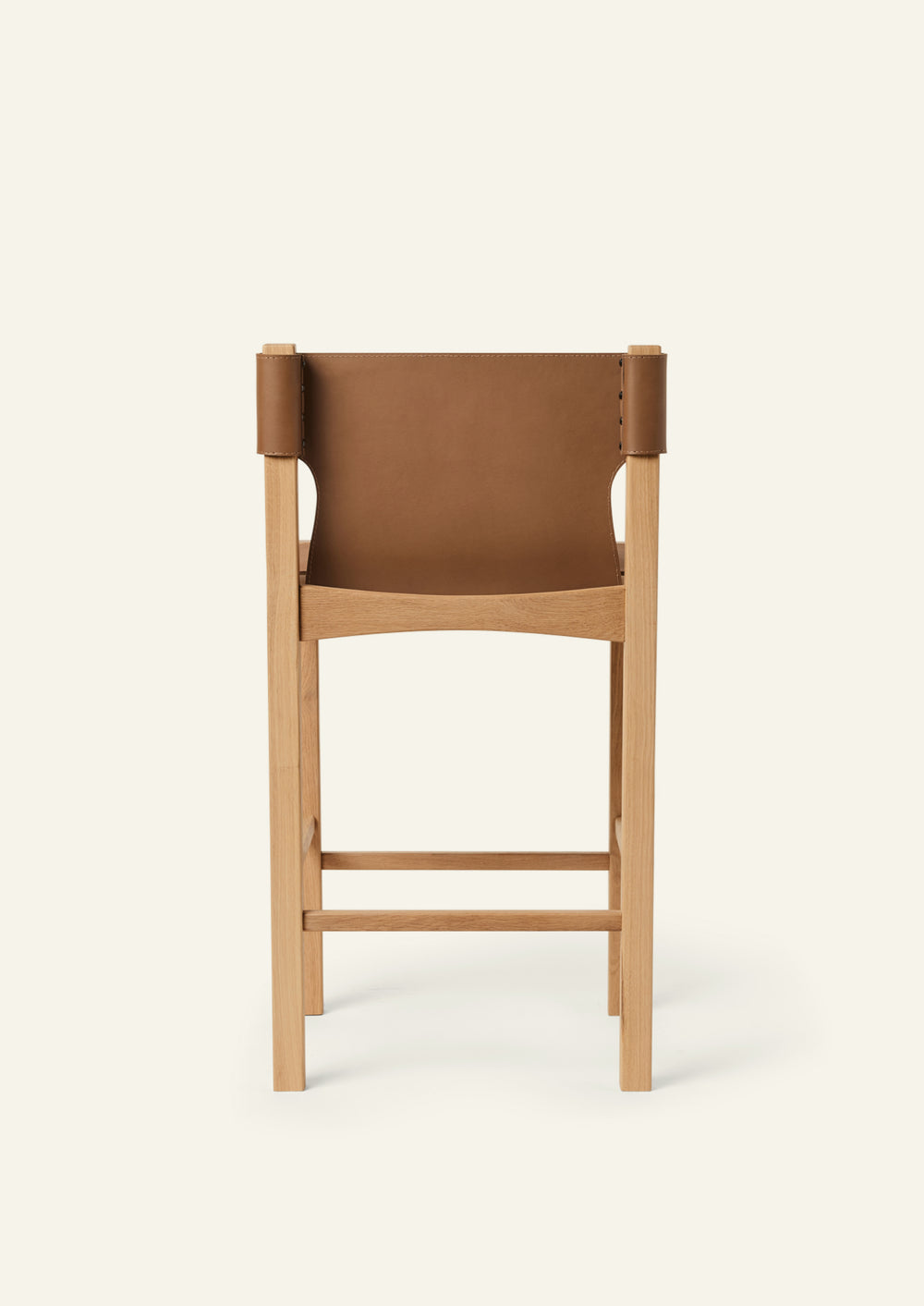 Rear view of the Henrik Counter Stool featuring a tailored leather backrest wrapped around the oak frame. The exposed wood structure and precise craftsmanship are visible from every angle.