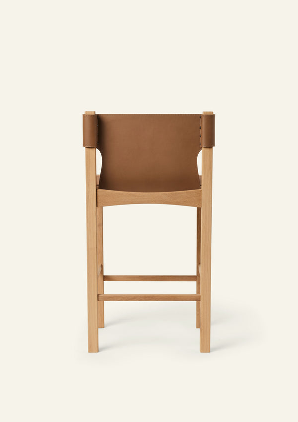 Rear view of the Henrik Counter Stool featuring a tailored leather backrest wrapped around the oak frame. The exposed wood structure and precise craftsmanship are visible from every angle.