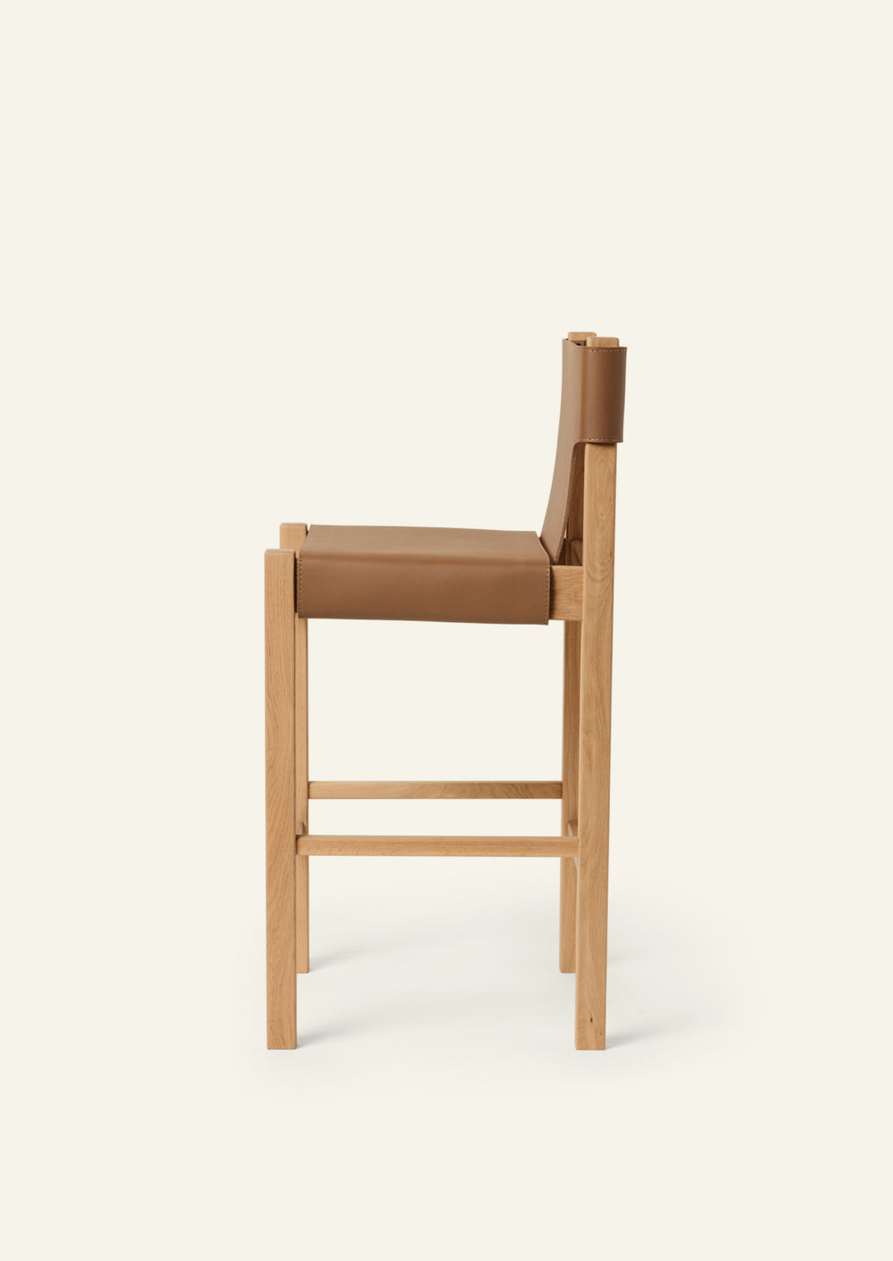 Side profile of the Henrik Counter Stool showcasing its streamlined proportions, supportive leather sling seat, and integrated footrests. The suspended leather construction creates a comfortable, refined seating experience.