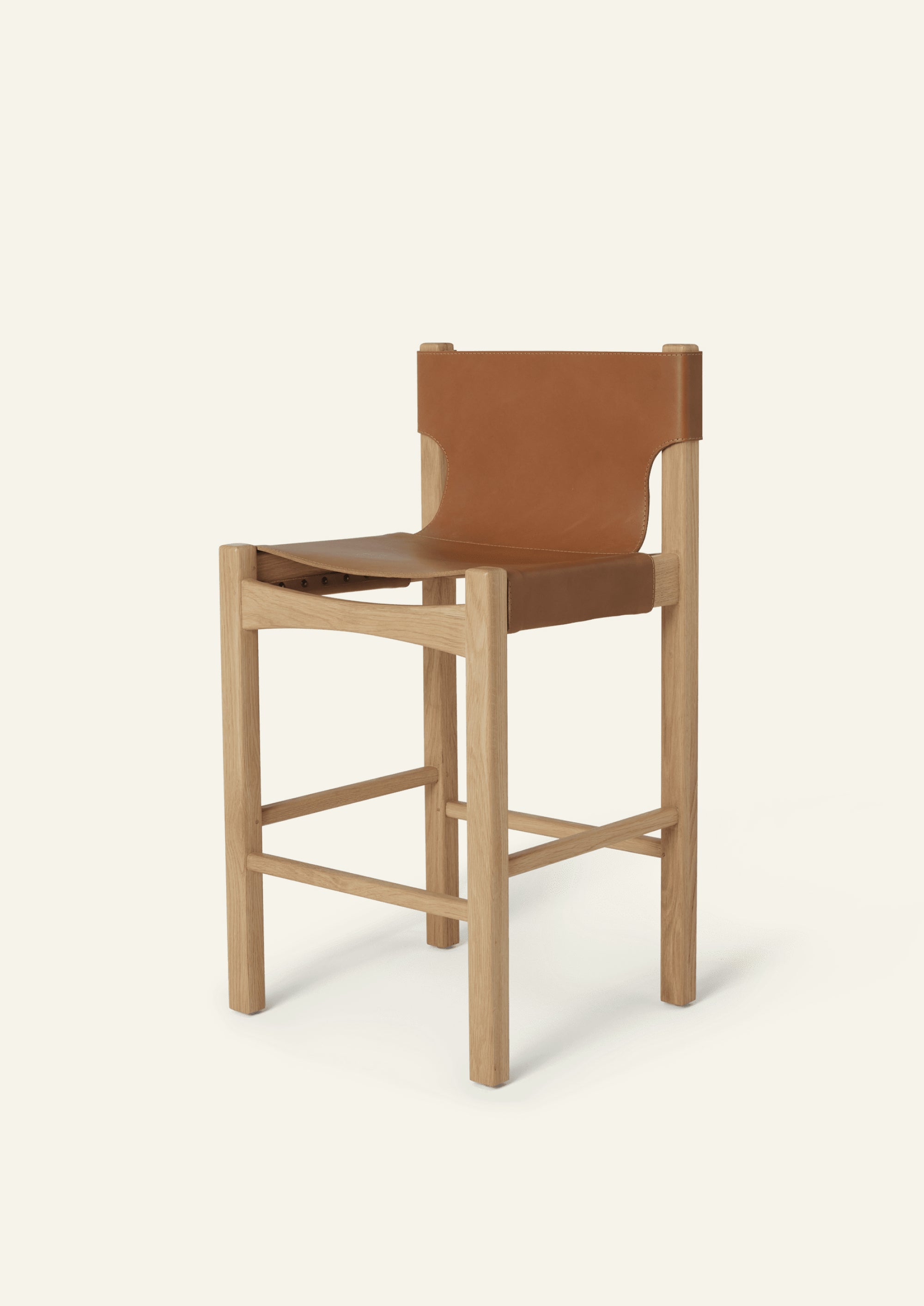 Three-quarter view of the Henrik Counter Stool featuring a solid white oak frame and suspended full-grain cognac leather seat and backrest. The elevated silhouette combines clean architectural lines with warm natural materials.