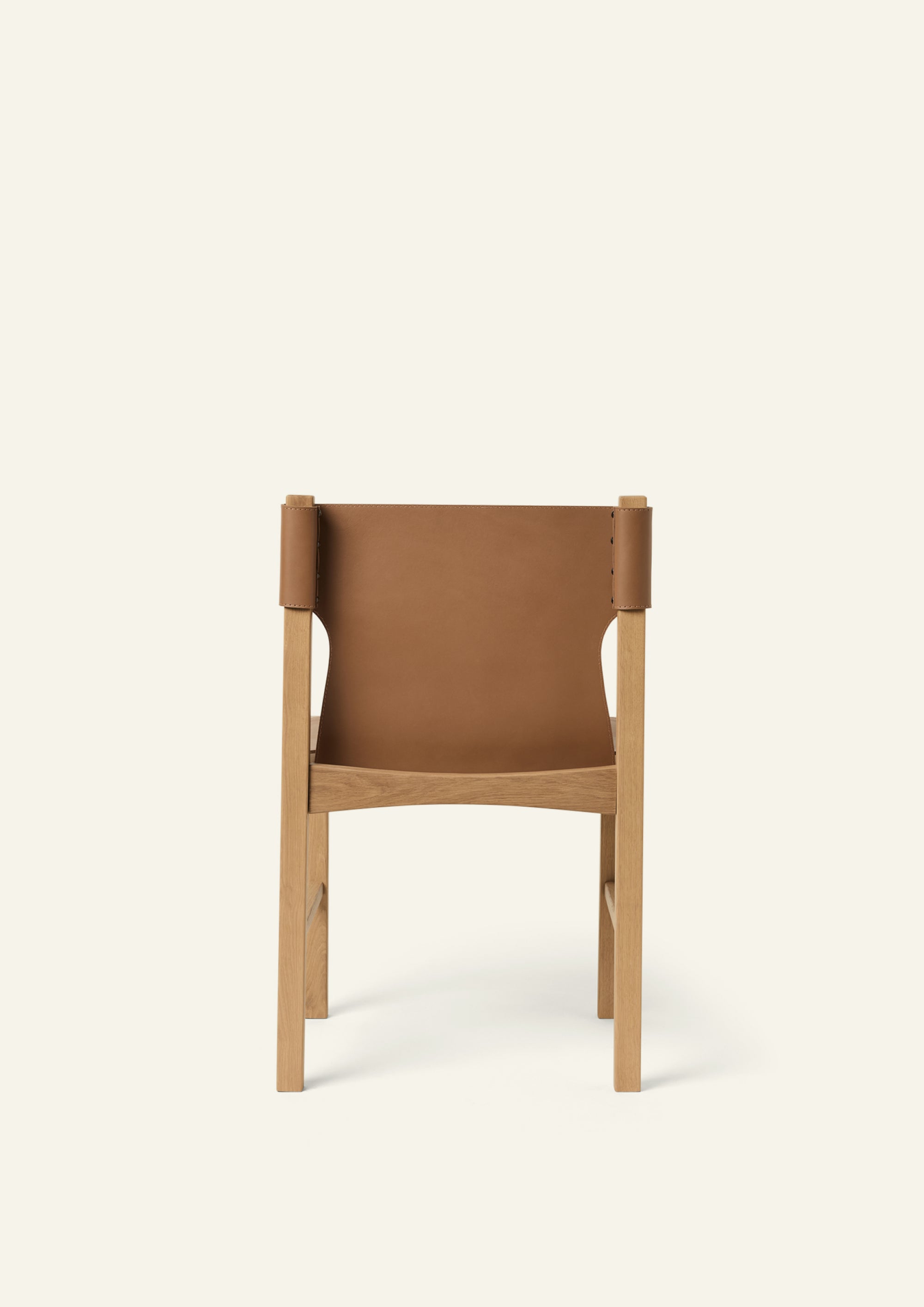 Rear view of the Henrik Dining Chair highlighting the sculptural leather backrest wrapped around the oak frame. The exposed wood structure and tailored leather detailing emphasize craftsmanship from every angle.