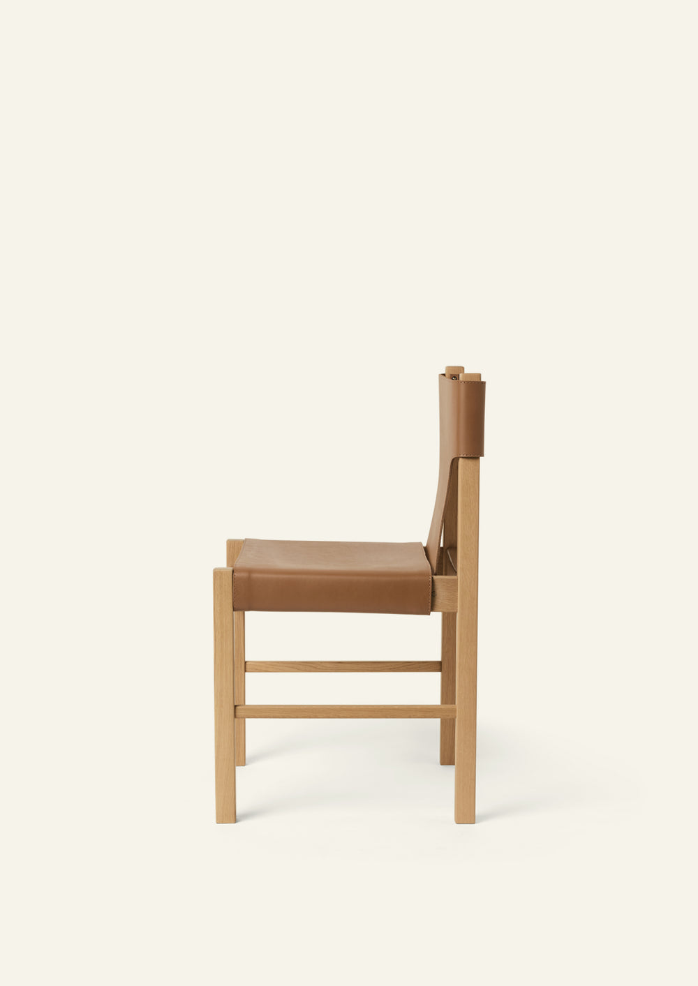 Side profile of the Henrik Dining Chair showcasing its slim proportions, suspended leather seat, and sturdy white oak frame. The gently curved leather provides comfort while maintaining a minimalist aesthetic.
