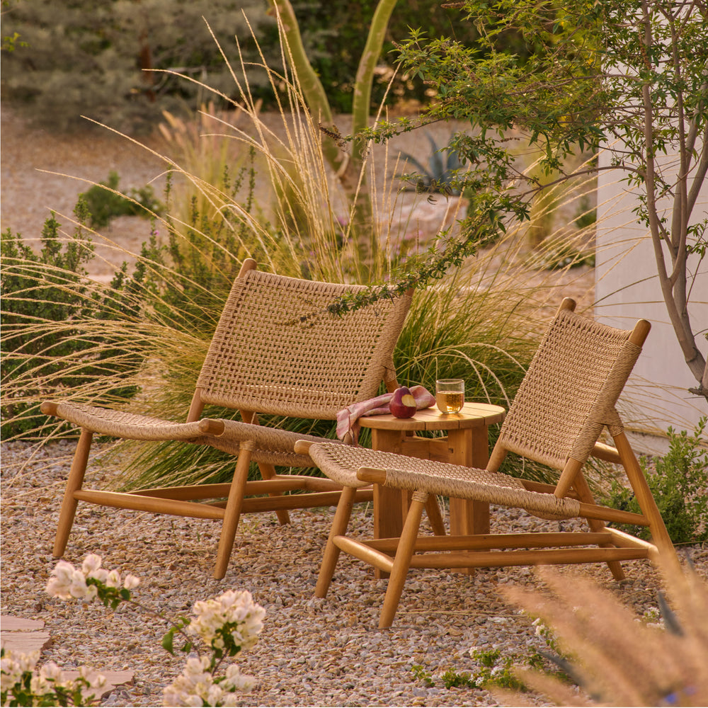 Two synthetic lounge (Bali Lounge) chairs and a small table (Otto Table) in a garden setting with plants and flowers.