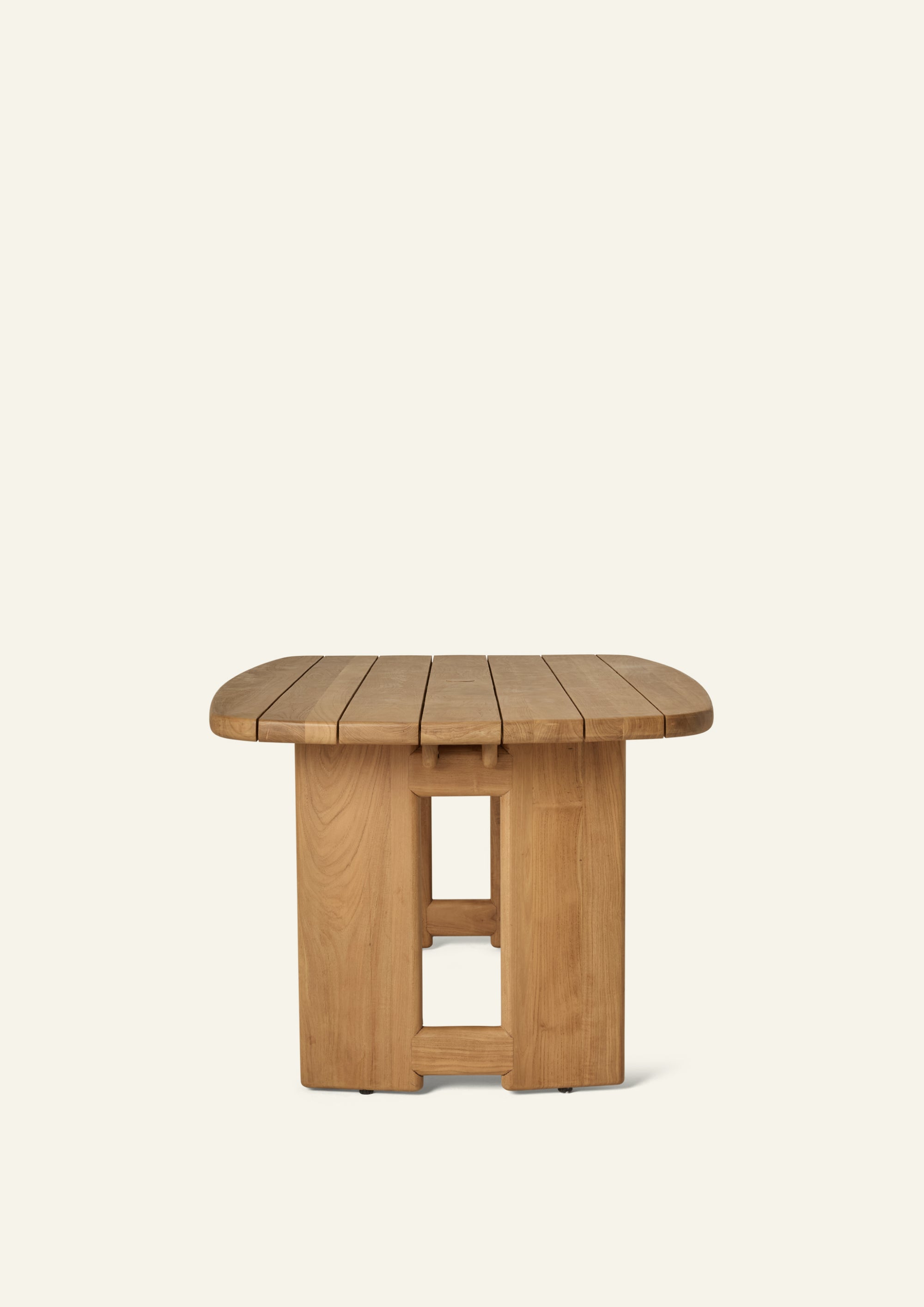 End view of the teak dining table highlighting its rounded rectangular slatted top and symmetrical pedestal supports. The clean lines and substantial proportions balance durability with refined outdoor style.