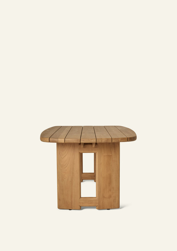 End view of the teak dining table highlighting its rounded rectangular slatted top and symmetrical pedestal supports. The clean lines and substantial proportions balance durability with refined outdoor style.