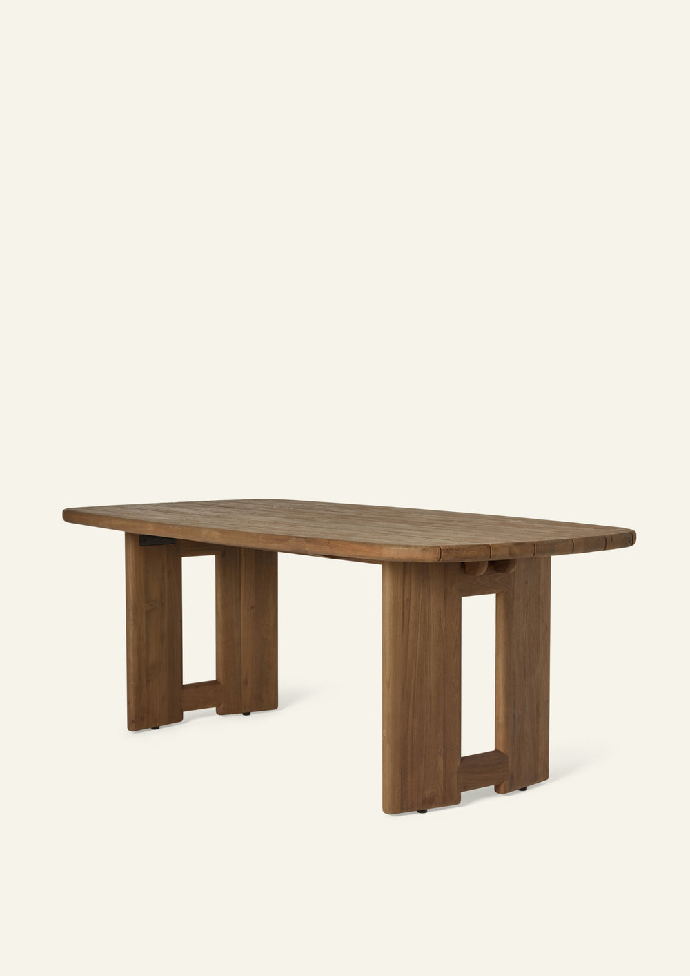 Three-quarter view of an outdoor dining table crafted from reclaimed teak. The rounded rectangular top features slatted construction for water drainage, while the architectural pedestal bases create a grounded silhouette suited for outdoor entertaining.