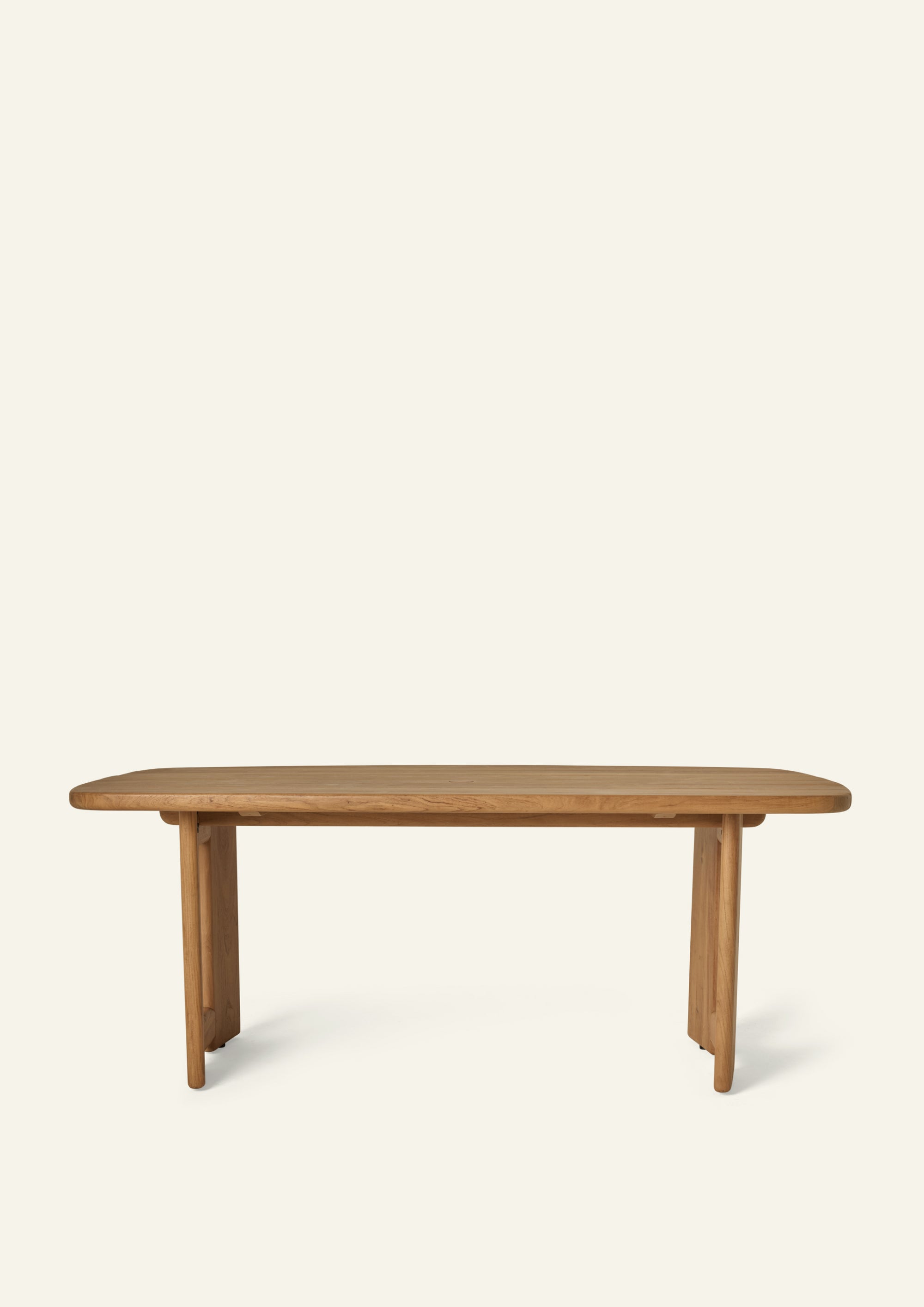Side profile of the teak dining table showcasing its elongated slatted top, rounded edges, and architectural pedestal supports. Designed for outdoor living, the slatted surface allows water to drain while maintaining a clean, sculptural appearance.