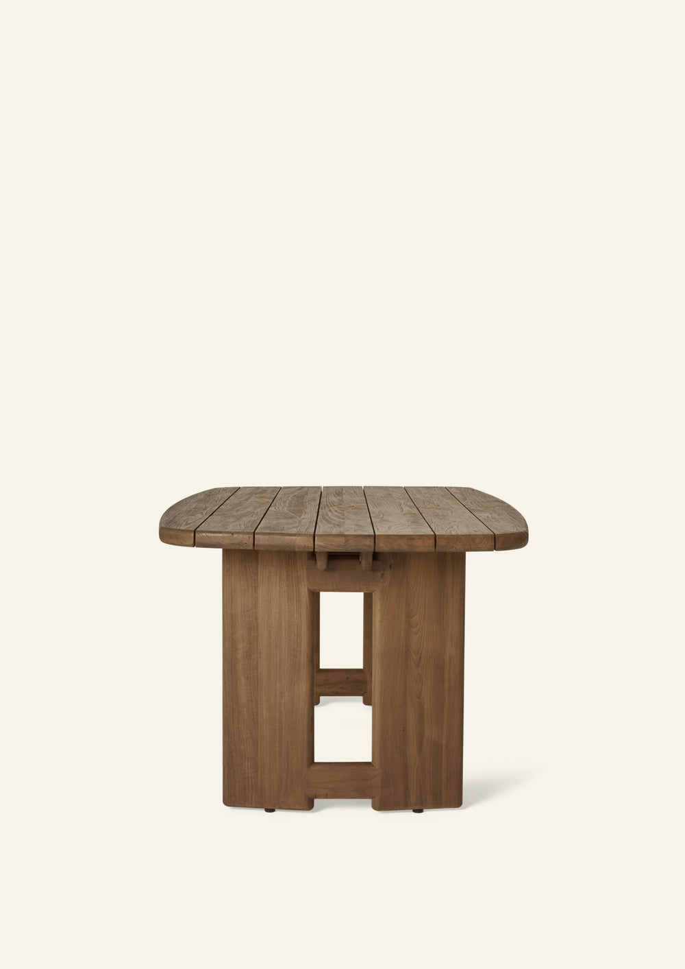 Side profile of the reclaimed teak dining table highlighting the slim tabletop, rounded edges, and architectural pedestal supports. The slatted construction allows rainwater to drain through while maintaining a refined, sculptural appearance.