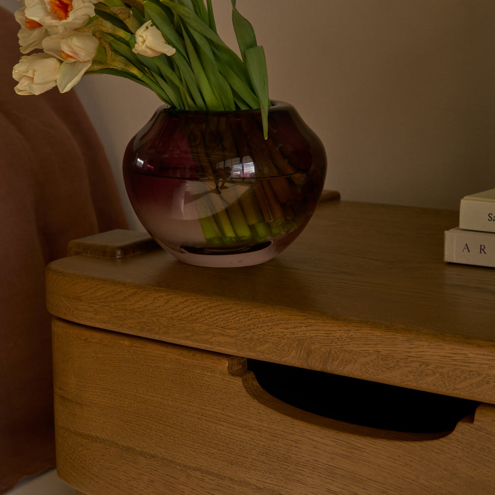 Cropped image of a vase with flowers on a honey oak nightstand.