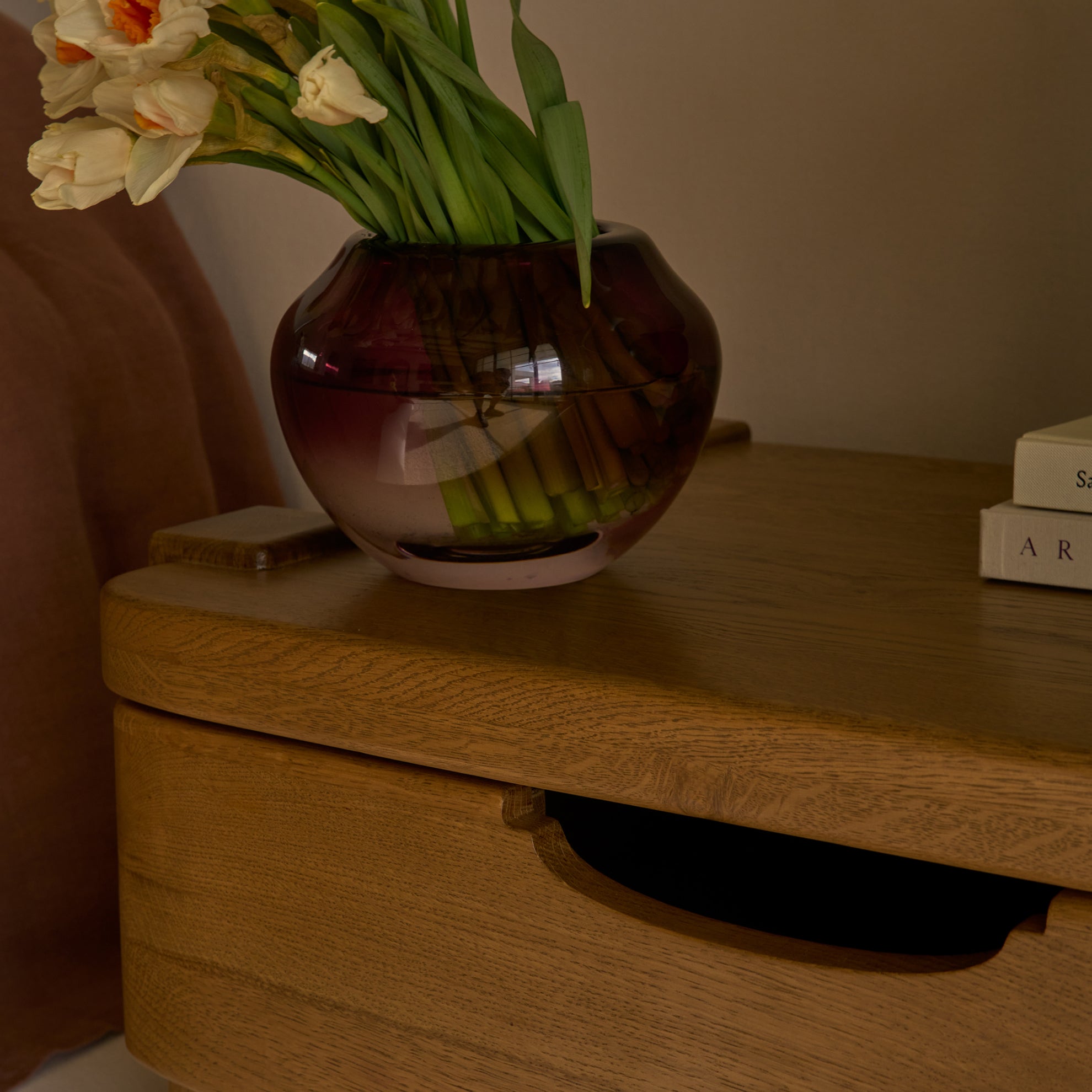 Cropped image of a vase with flowers on a honey oak nightstand.