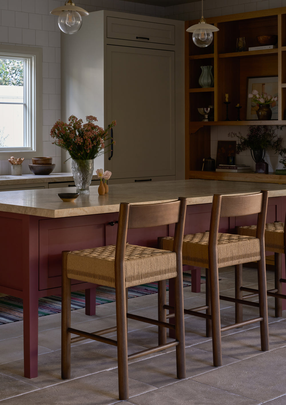 Brown oak counter stool in a transitional style kitchen with a mauve kitchen island, florals and decor elements in the background. 