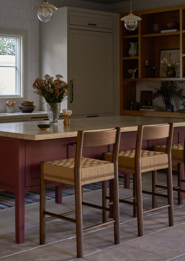 A row of Isa Counter Stools lines a mauve kitchen island, bringing warmth, texture, and natural materials to the heart of the home.