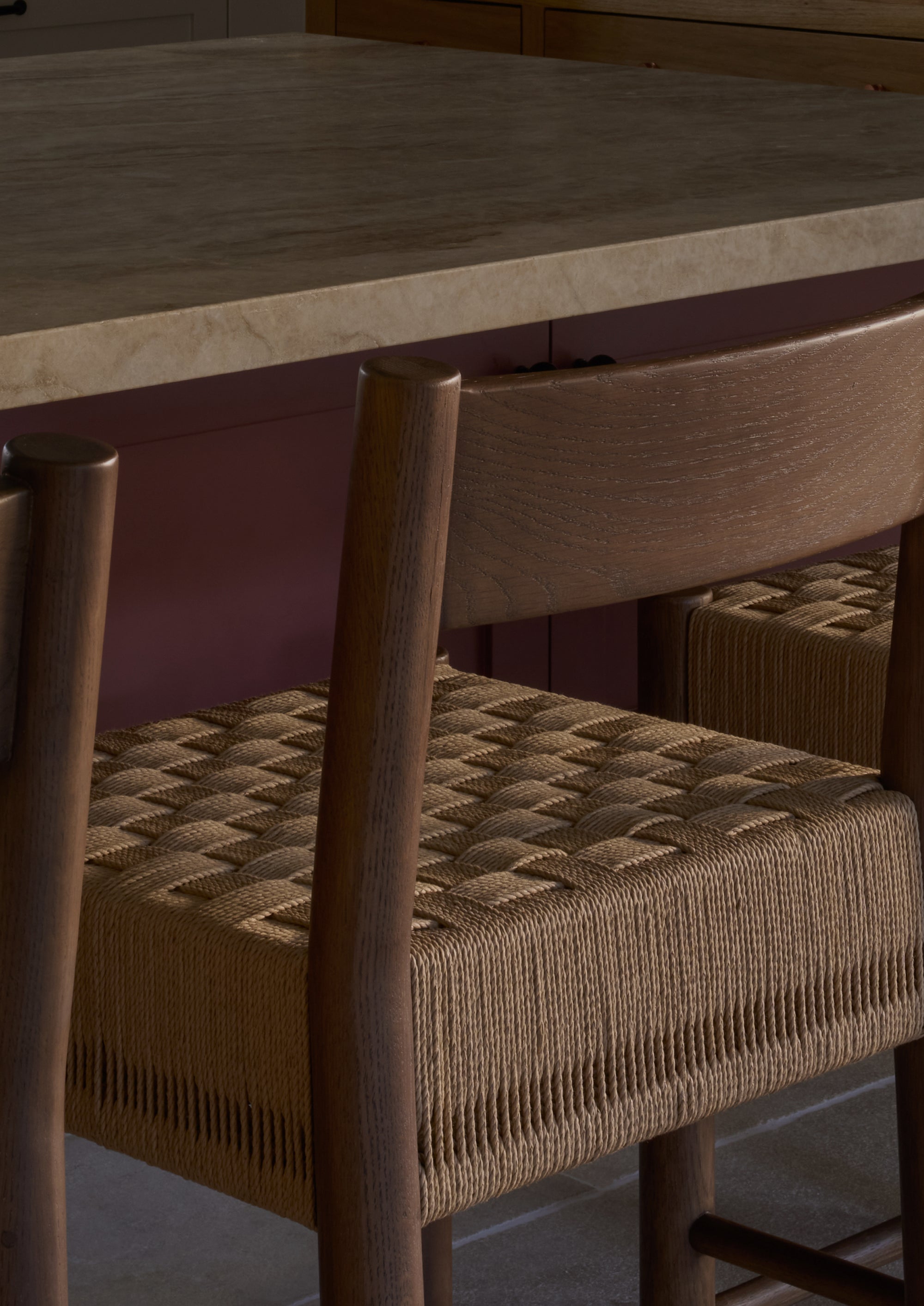 Close-up of the Isa Counter Stool tucked beneath a kitchen island, highlighting the contrast between the rich brown oak frame and checker-board woven seat.