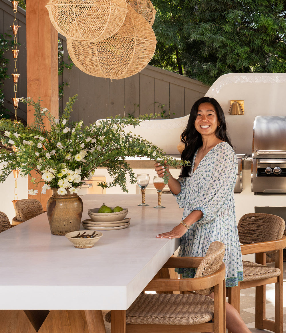 Woman arranging flowers in a modern outdoor kitchen setting with plaster dining table and Vera dining chairs. 