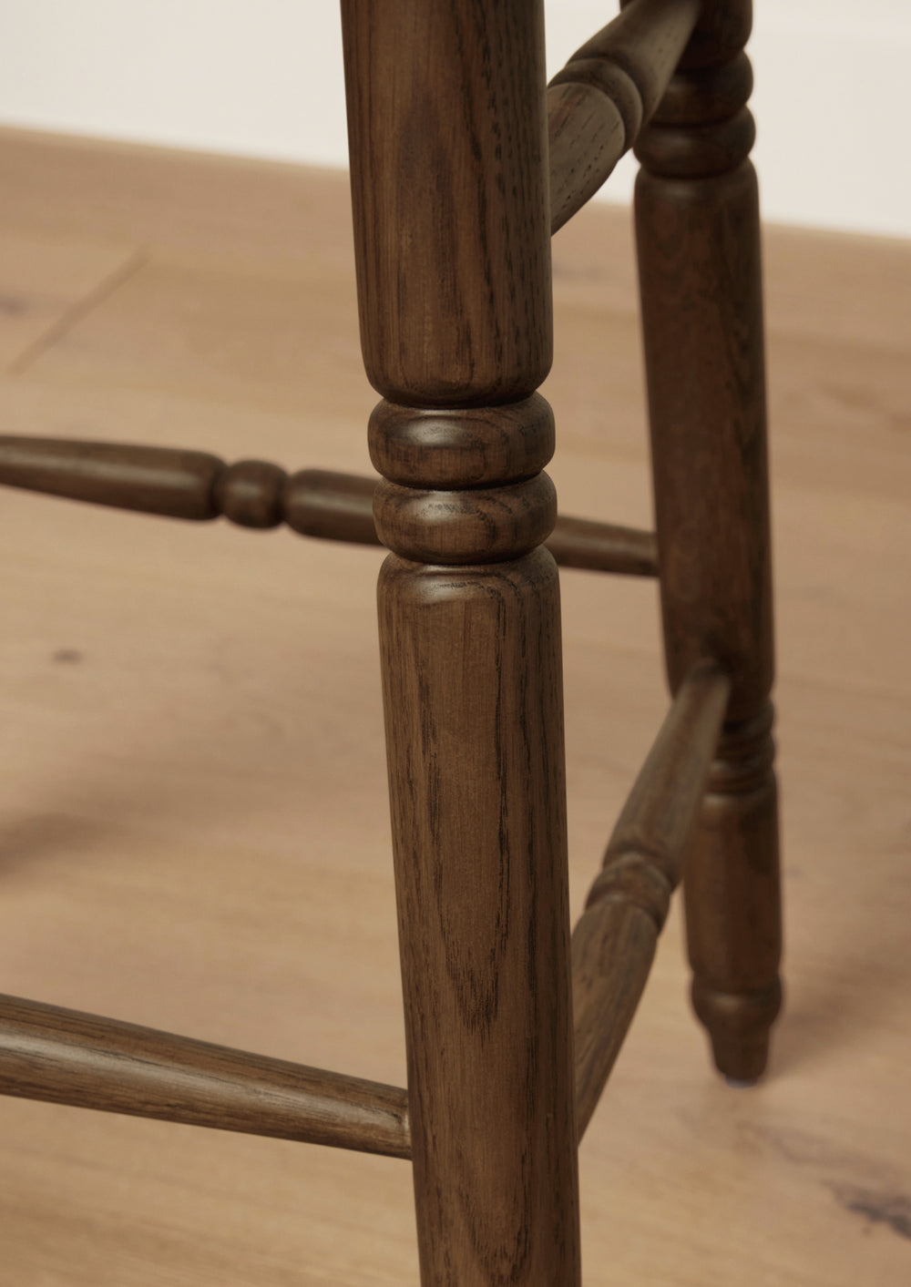 Close-up of the stool’s hand-turned oak leg detailing and stretcher joinery. The rich brown finish highlights the natural wood grain and craftsmanship.