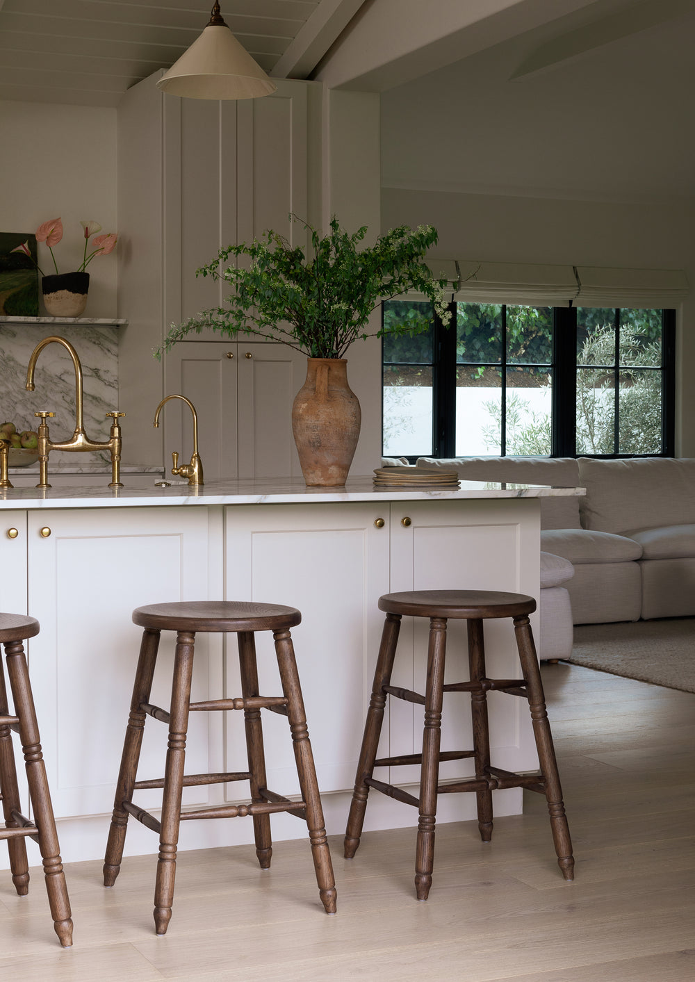 Solid oak counter stools gathered around a bright kitchen island with marble countertops and brass fixtures. The rich brown finish adds warmth and complements both traditional and modern interiors.