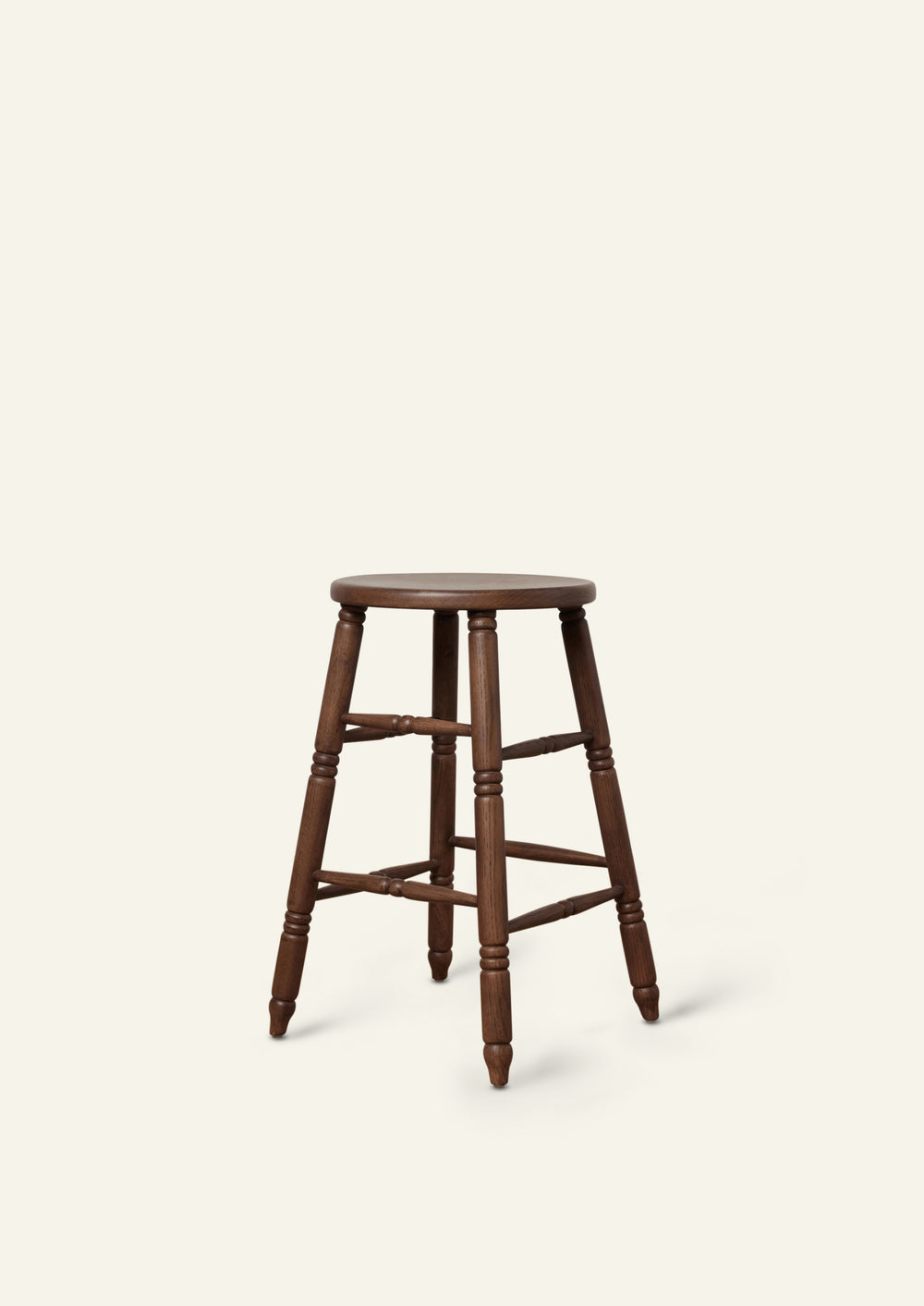 Three-quarter view of a classic counter stool crafted from solid brown oak. Hand-turned legs and stretchers lend traditional character, while the dark wood finish gives the piece a warm, refined presence.