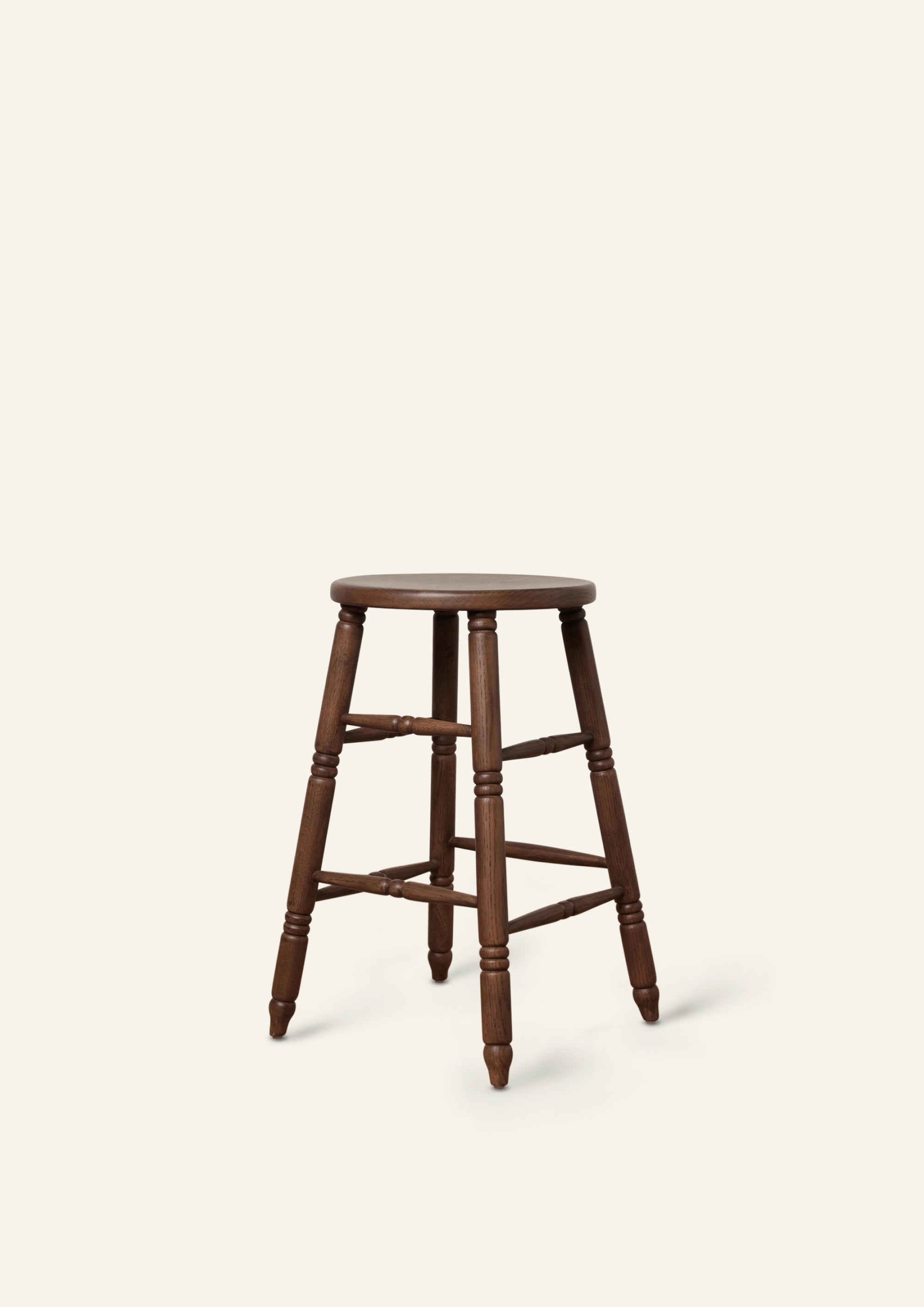 Three-quarter view of a classic counter stool crafted from solid brown oak. Hand-turned legs and stretchers lend traditional character, while the dark wood finish gives the piece a warm, refined presence.