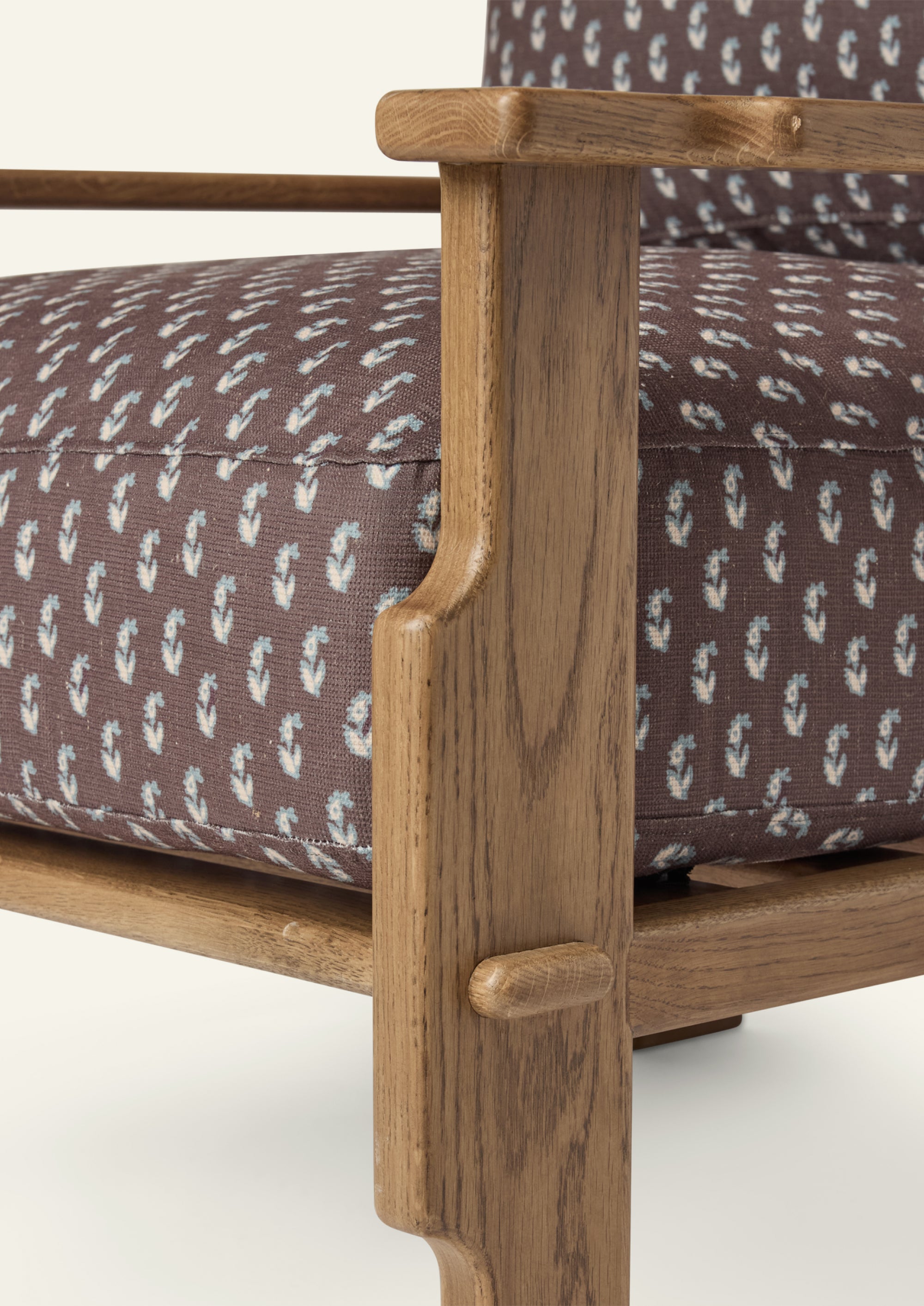 Close-up of the lounge chair arm and frame, highlighting the honey oak finish, sculpted joinery details, and brown floral upholstery featuring a delicate floral motif.