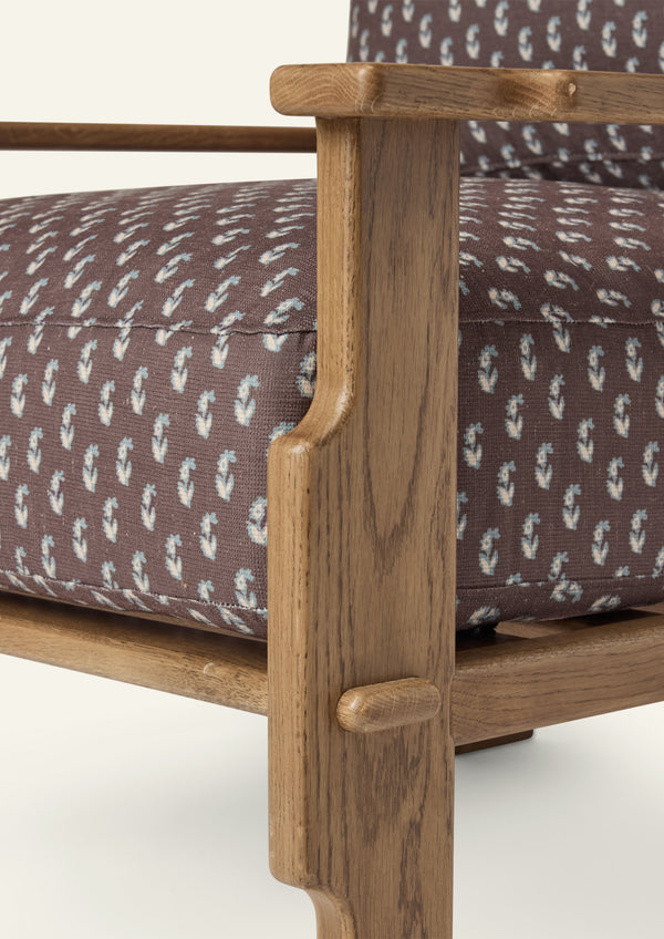 Close-up of the lounge chair arm and frame, highlighting the honey oak finish, sculpted joinery details, and brown floral upholstery featuring a delicate floral motif.