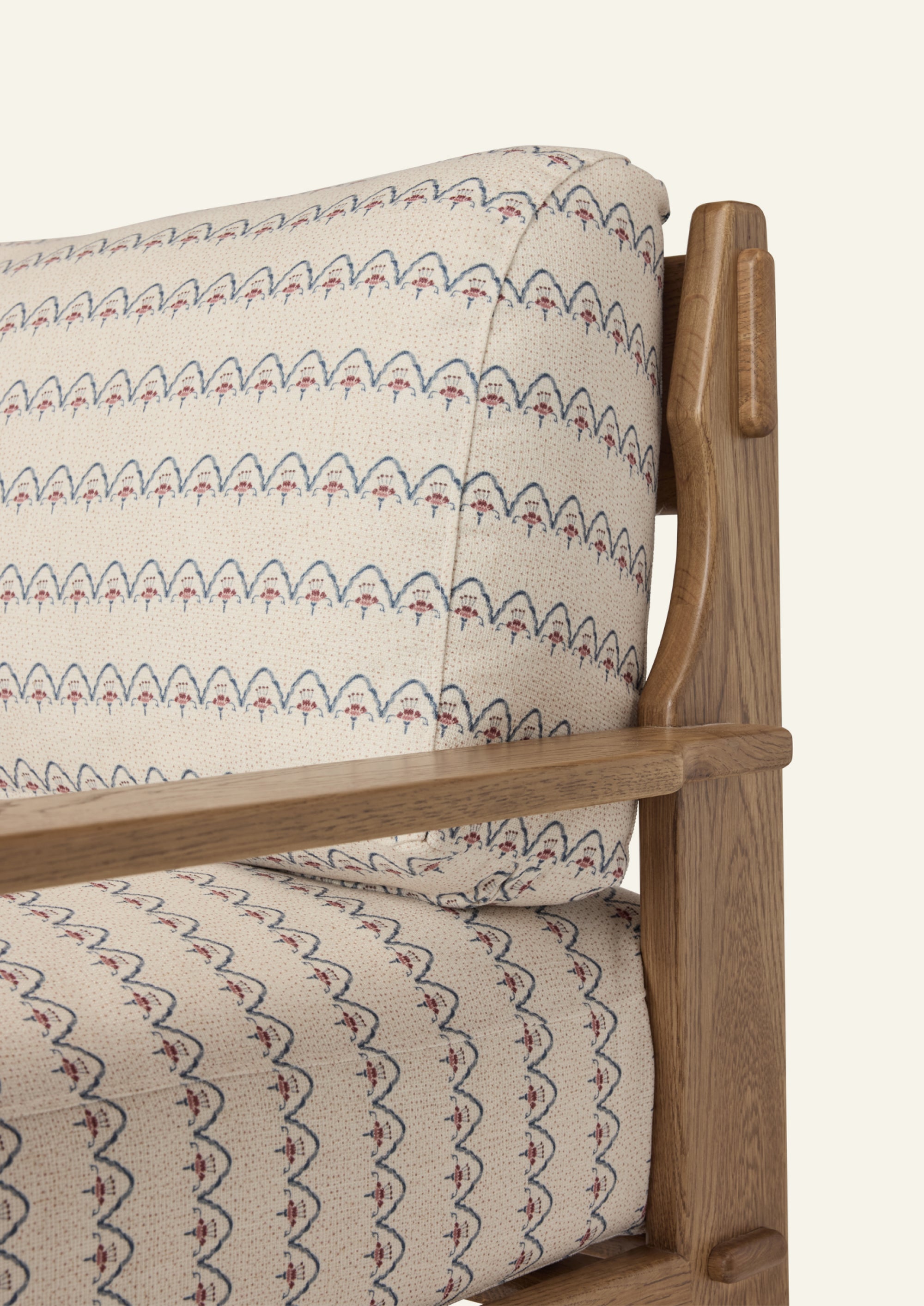 Close-up of the lounge chair arm and frame, highlighting the honey oak finish, sculptural joinery, and Neutral Arches upholstery with its delicate blue and blush motif on an ivory ground.