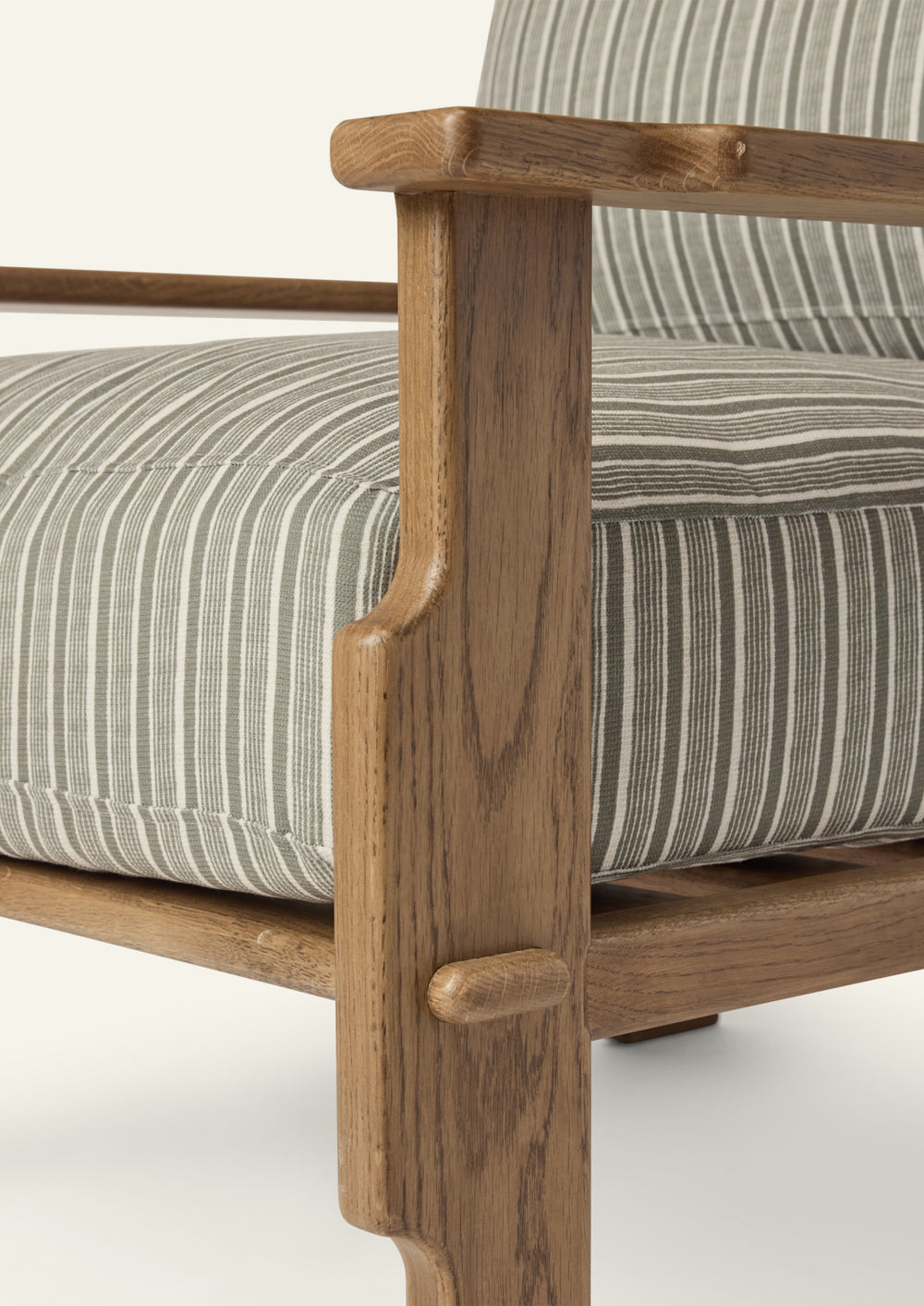 Close-up of the lounge chair arm and frame, highlighting the warm honey oak finish, sculpted joinery details, and green stripe upholstery with subtle woven texture.