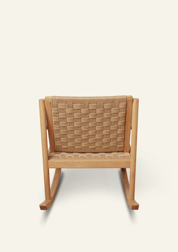 Rear view of a natural oak rocking chair showcasing the woven paper cord backrest. The basketweave pattern highlights the craftsmanship and texture of the handwoven material, framed by a solid oak structure.