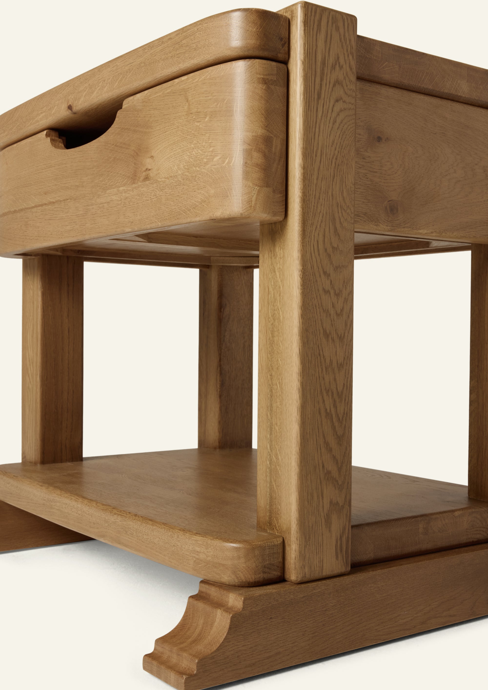 Close-up of the nightstand’s solid oak frame, showcasing rounded corners, substantial joinery, open lower shelf, and decorative bracket foot detailing. The natural wood grain highlights the craftsmanship and durability of the piece.