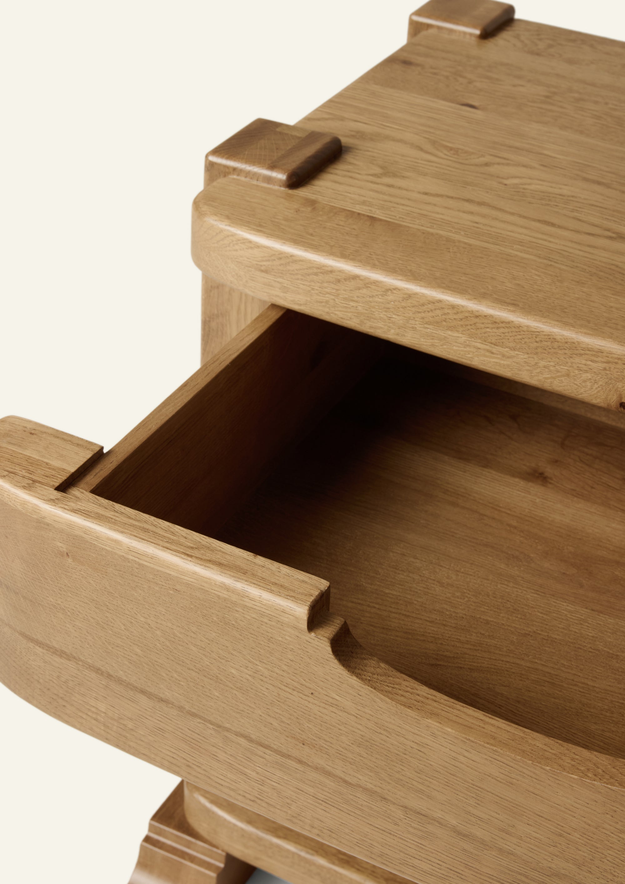 Close-up of the nightstand with the drawer partially open, revealing spacious storage. Rounded edges, integrated finger pull, and visible oak grain emphasize the handcrafted character of the design.