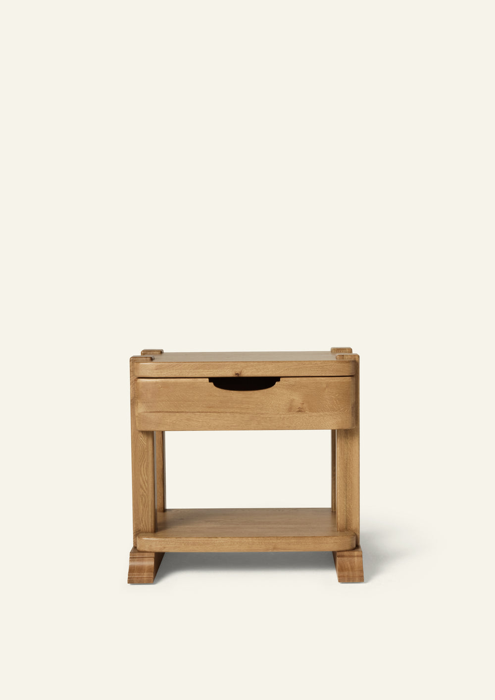 Front view of a honey oak nightstand featuring a single drawer with an integrated pull, open lower shelf, and sculpted bracket feet. Shown against a soft ivory background, the design highlights the natural beauty of solid oak construction.