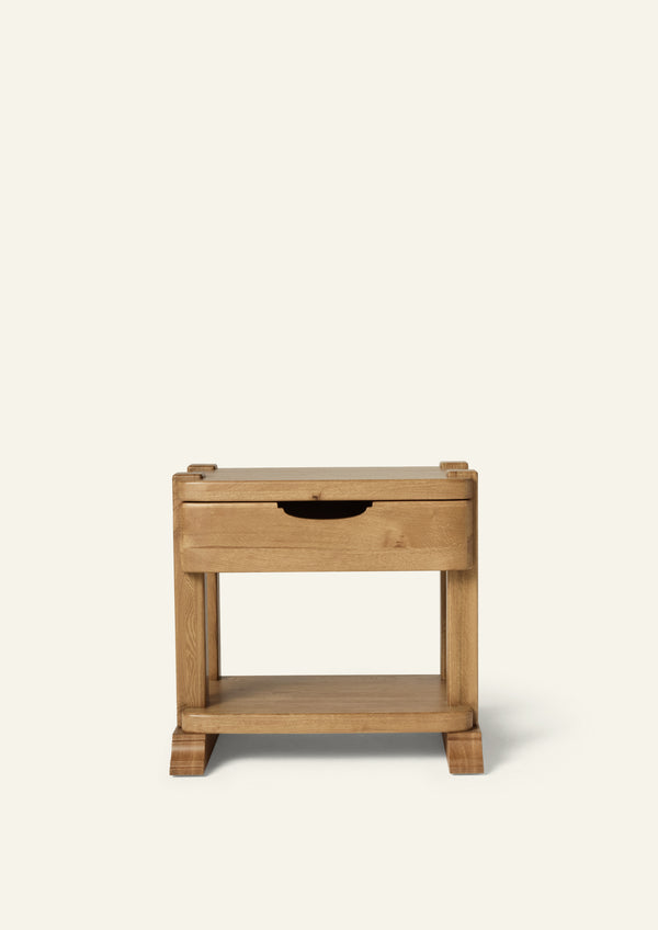 Front view of a honey oak nightstand featuring a single drawer with an integrated pull, open lower shelf, and sculpted bracket feet. Shown against a soft ivory background, the design highlights the natural beauty of solid oak construction.