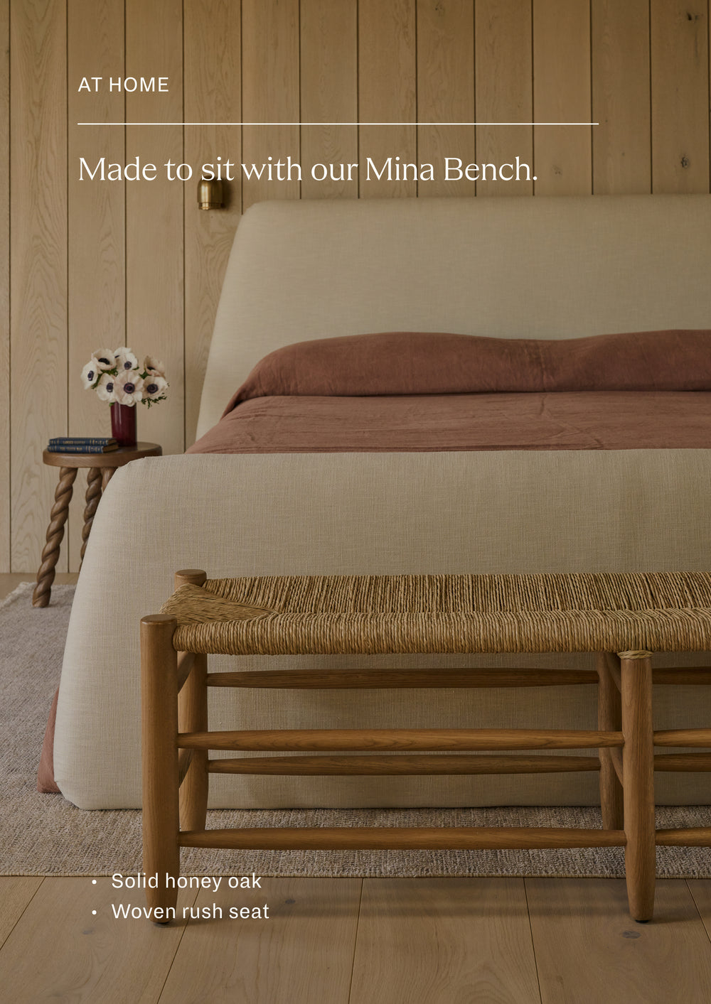 Made to sit with our Mina Bench. Bedroom featuring a woven rush bench at the foot of an upholstered bed, styled with warm neutral bedding and natural wood finishes. The image highlights the coordinated materials and craftsmanship shared across the collection.