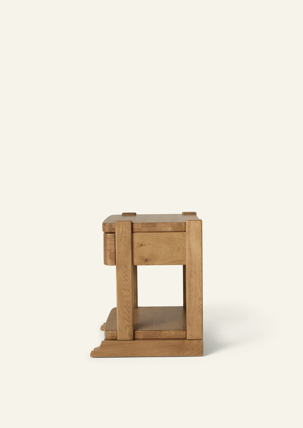 Side profile of the honey oak nightstand showing its thick solid oak frame, drawer construction, open lower shelf, and decorative bracket base. The streamlined silhouette balances traditional detailing with clean lines.