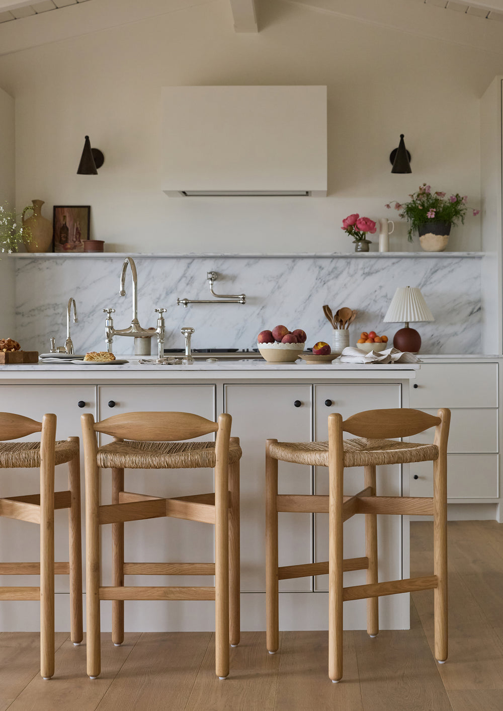 Lifestyle image of a modern European style kitchen with the Olma Counter stool–a white oak counter stool with a low profile back and natural rush seat. 