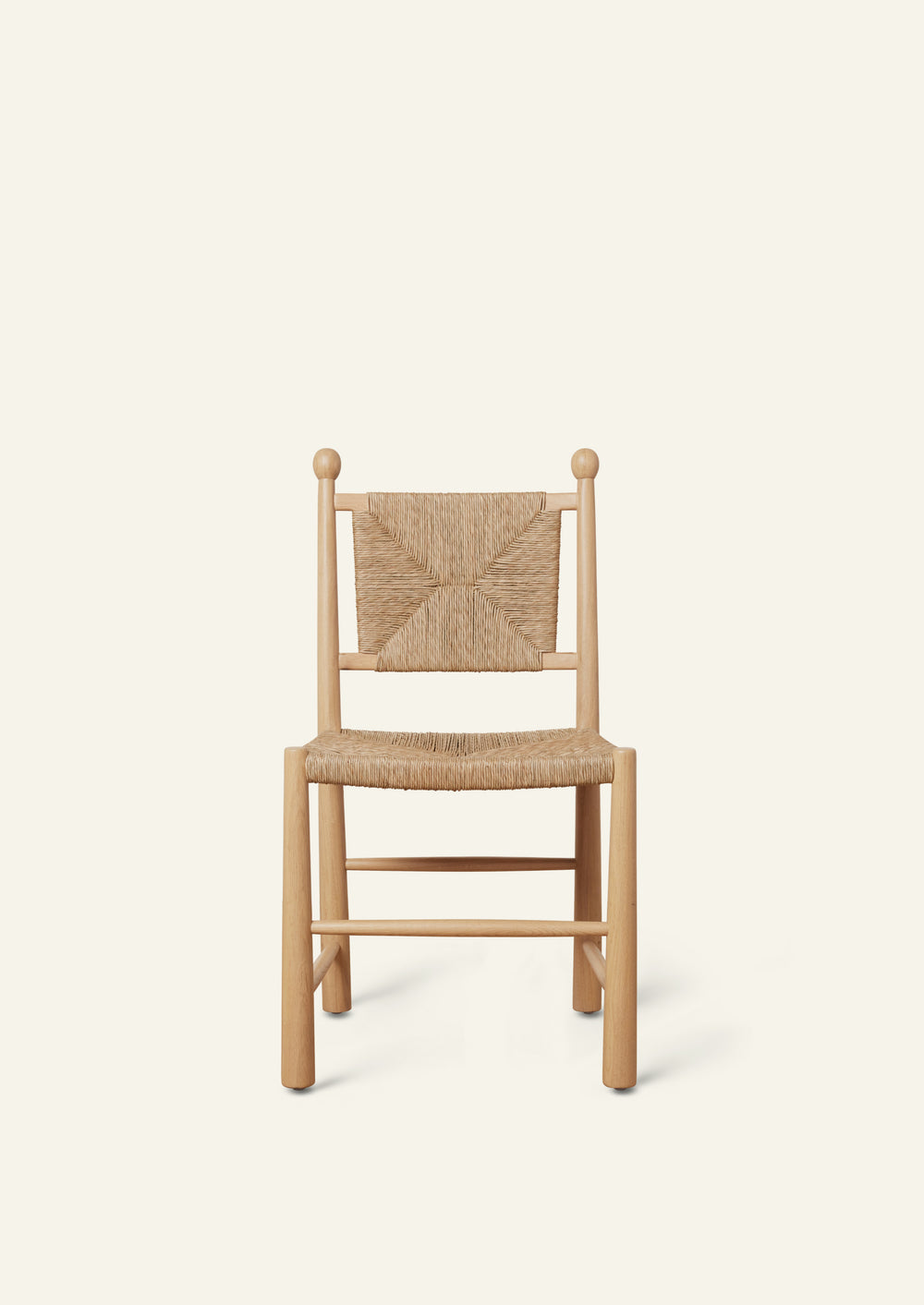 Front view of a white oak dining chair featuring a handwoven rush seat and geometric woven backrest. The chair has rounded legs, simple stretcher supports, and decorative finials atop the back posts, shown against a warm ivory backdrop.