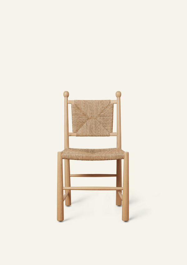 Front view of a white oak dining chair featuring a handwoven rush seat and geometric woven backrest. The chair has rounded legs, simple stretcher supports, and decorative finials atop the back posts, shown against a warm ivory backdrop.