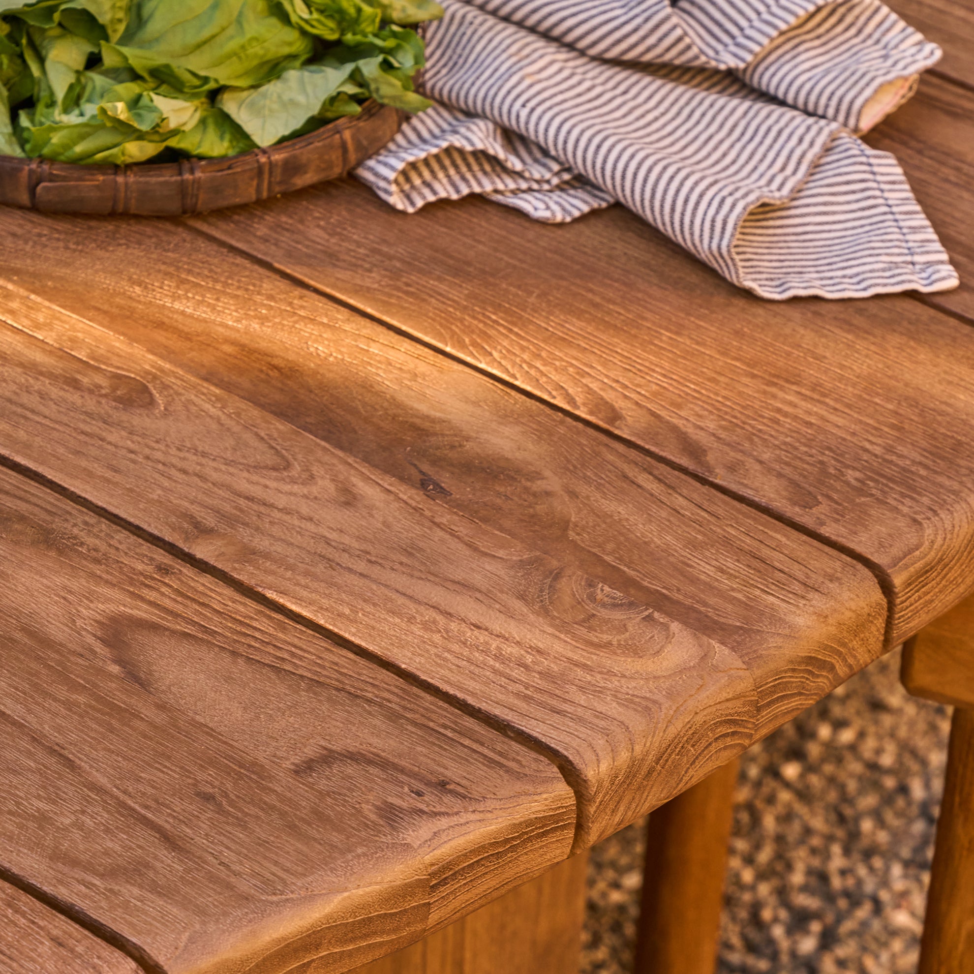 Reclaimed teak table with a basket of green leaves and a striped cloth on a natural background