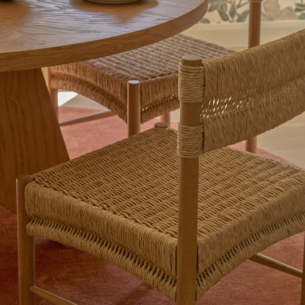 Wooden dining table with natural rush chairs on a blush pink carpet