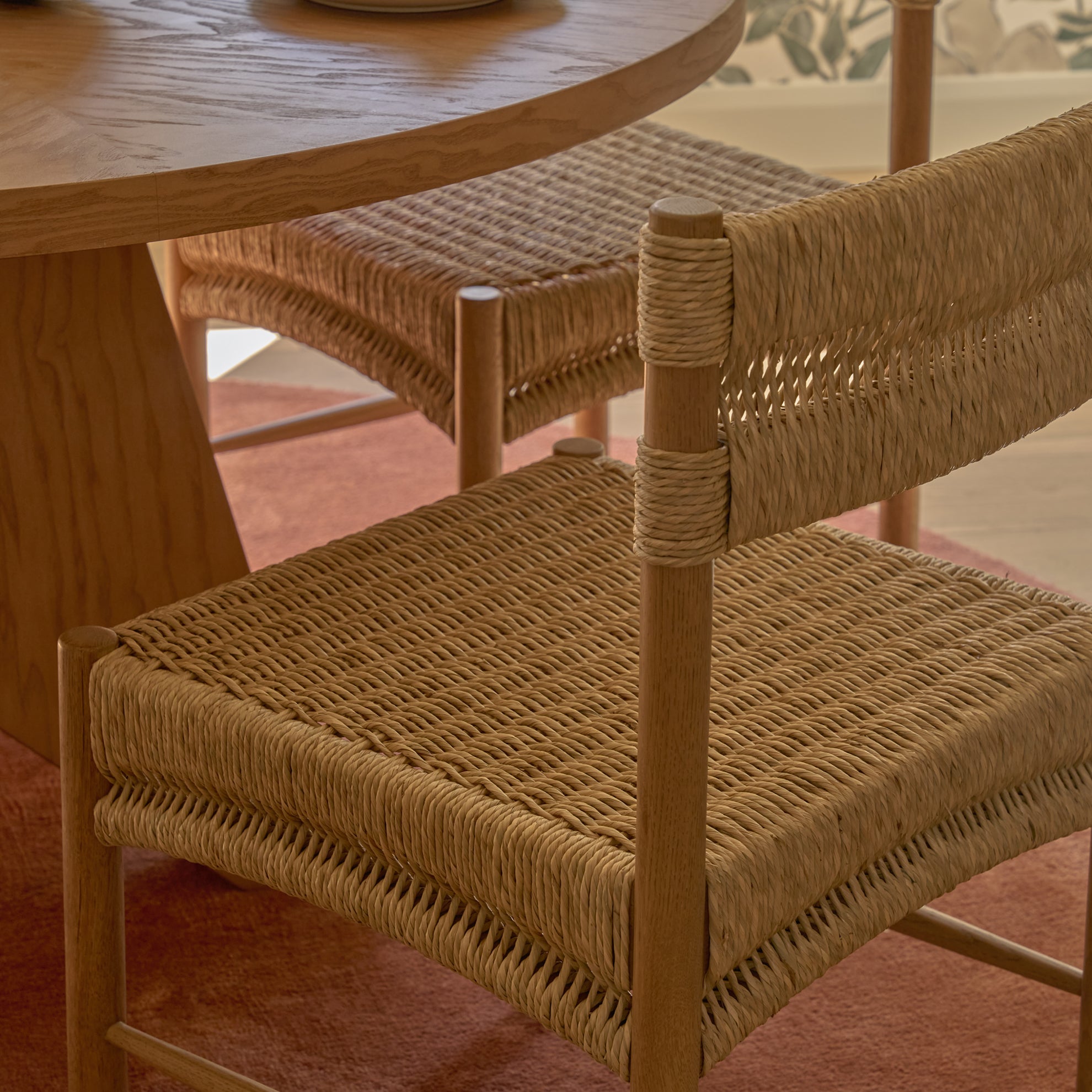 Wooden dining table with natural rush chairs on a blush pink carpet