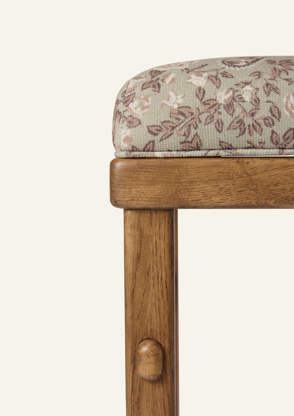 Close-up of the counter stool highlighting the sage floral upholstery and warm honey oak frame. The softly textured fabric features delicate floral motifs in sage, taupe, and blush tones, paired with handcrafted wood detailing.