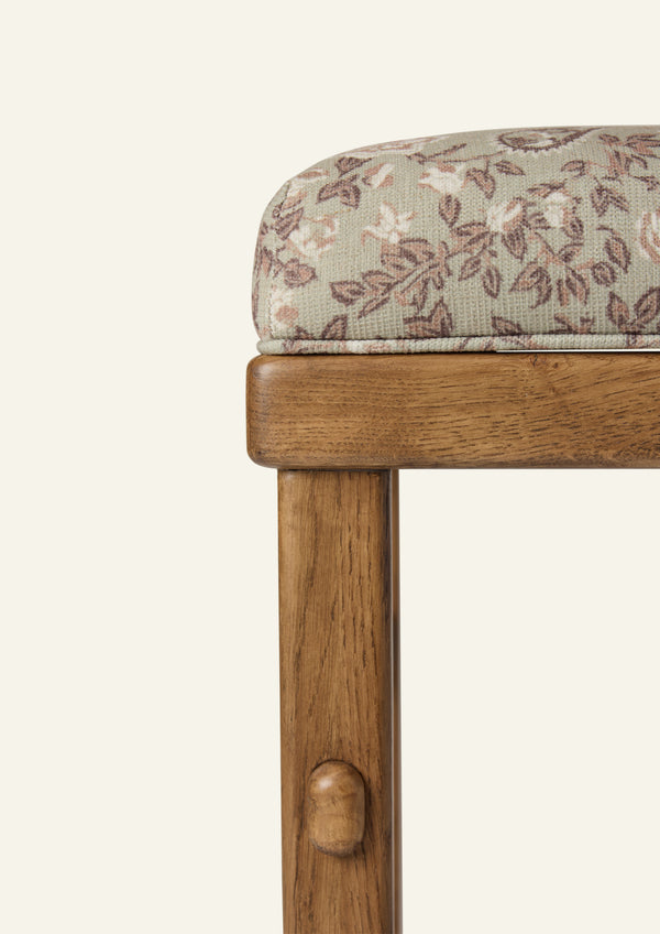 Close-up of the counter stool highlighting the sage floral upholstery and warm honey oak frame. The softly textured fabric features delicate floral motifs in sage, taupe, and blush tones, paired with handcrafted wood detailing.